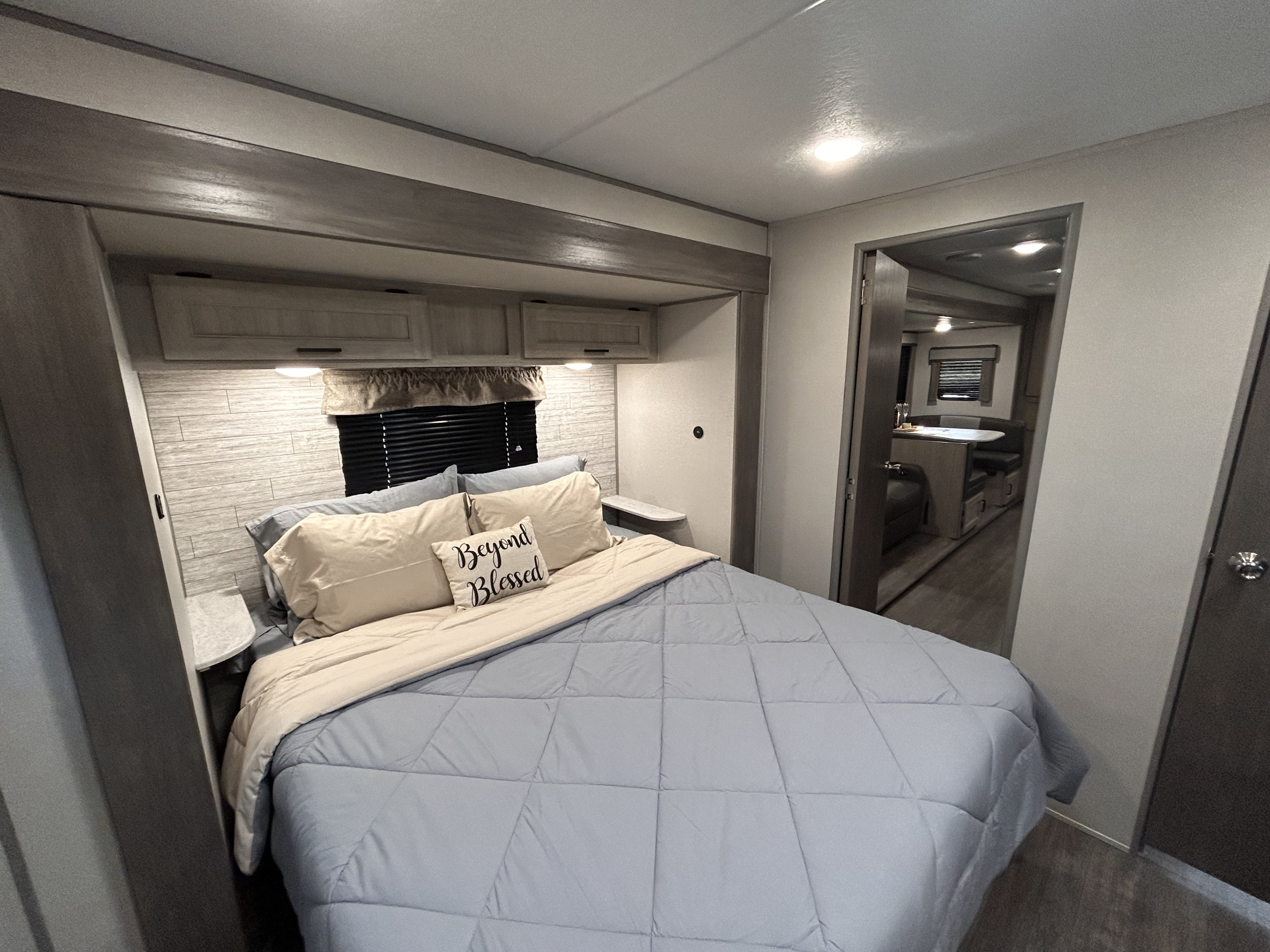 Cozy RV rental bedroom with light blue bedding, wood-look wall, and view of the dinette.. Forest River 26FKDS 2025