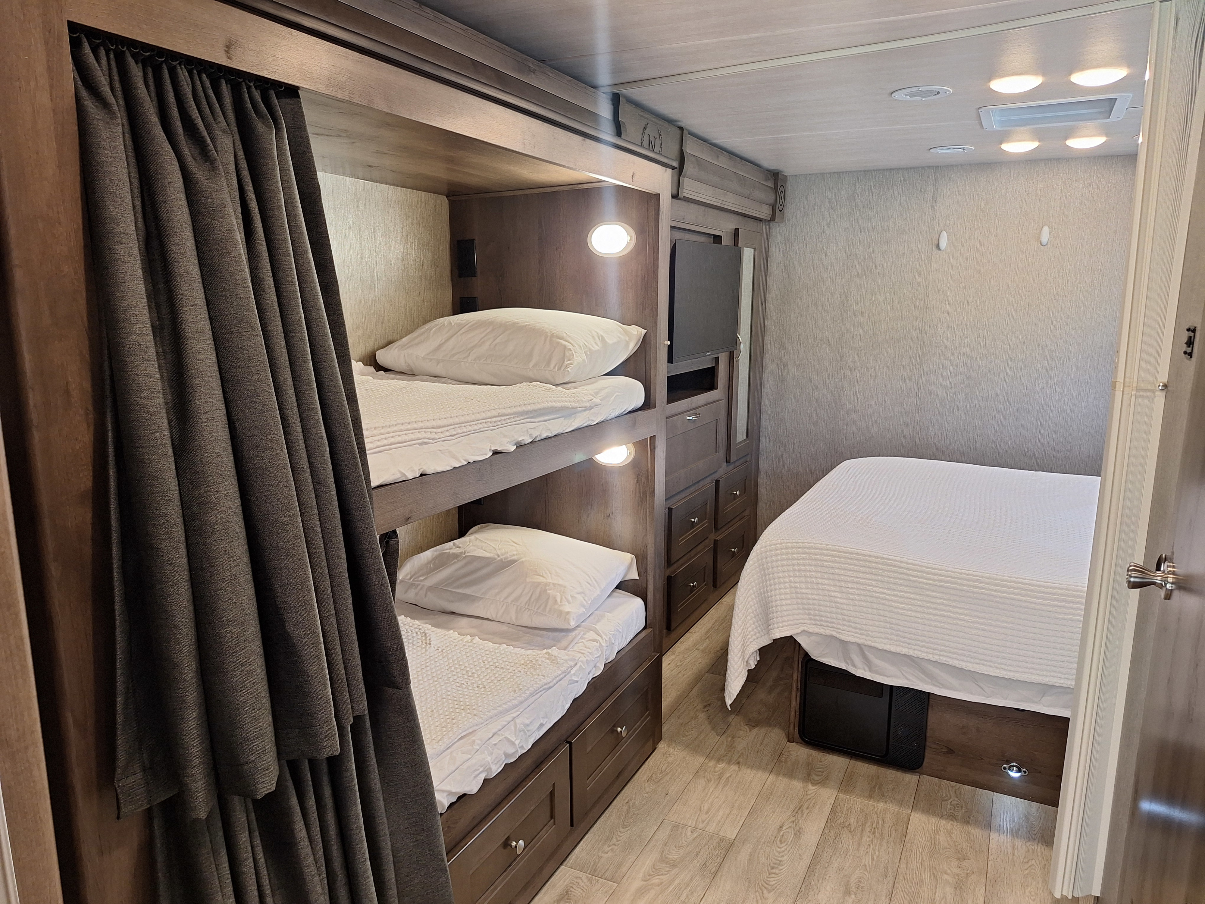 Cozy rv rental bedroom showing bunk beds with privacy curtains, a master bed, and storage. Ideal for travelers.. Nexus Phantom 2024