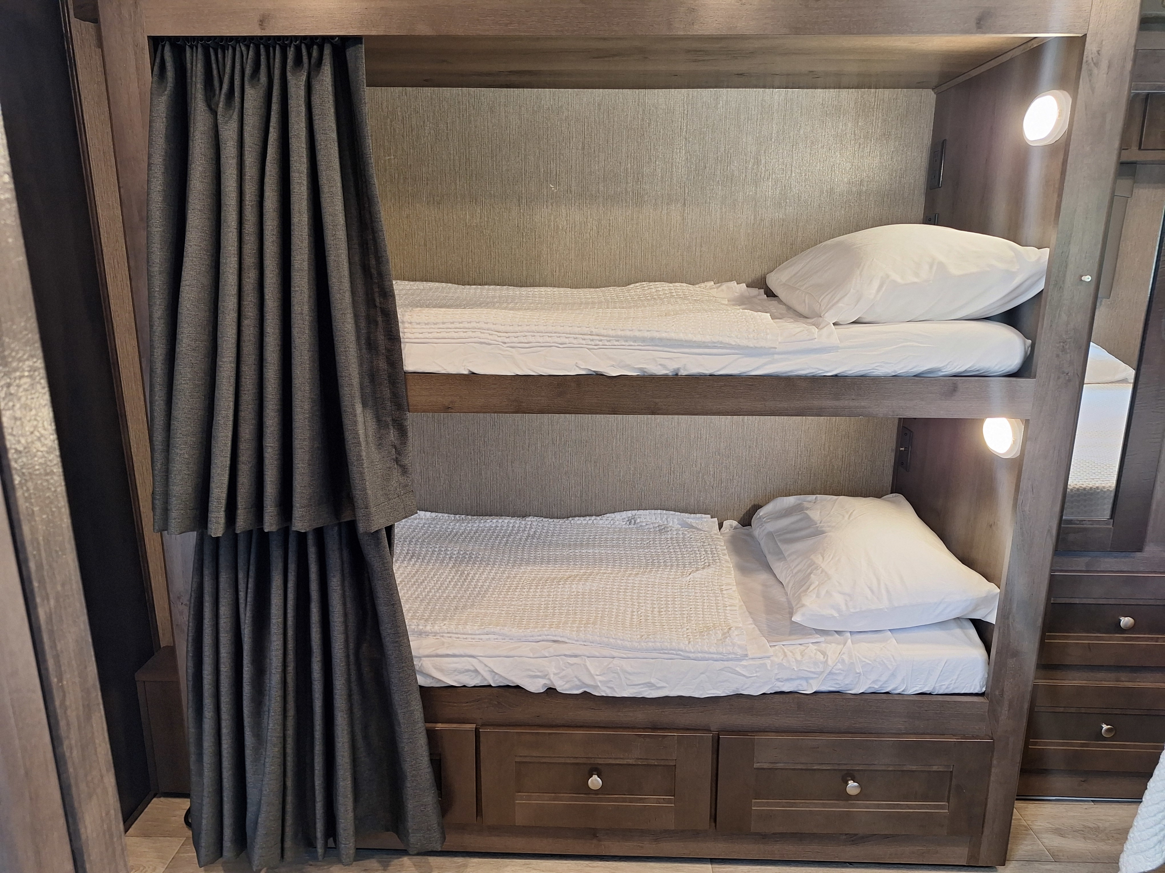 RV rental interior: stacked bunk beds with fresh white bedding, privacy curtains, individual lights, and under-bunk storage.. Nexus Phantom 2024