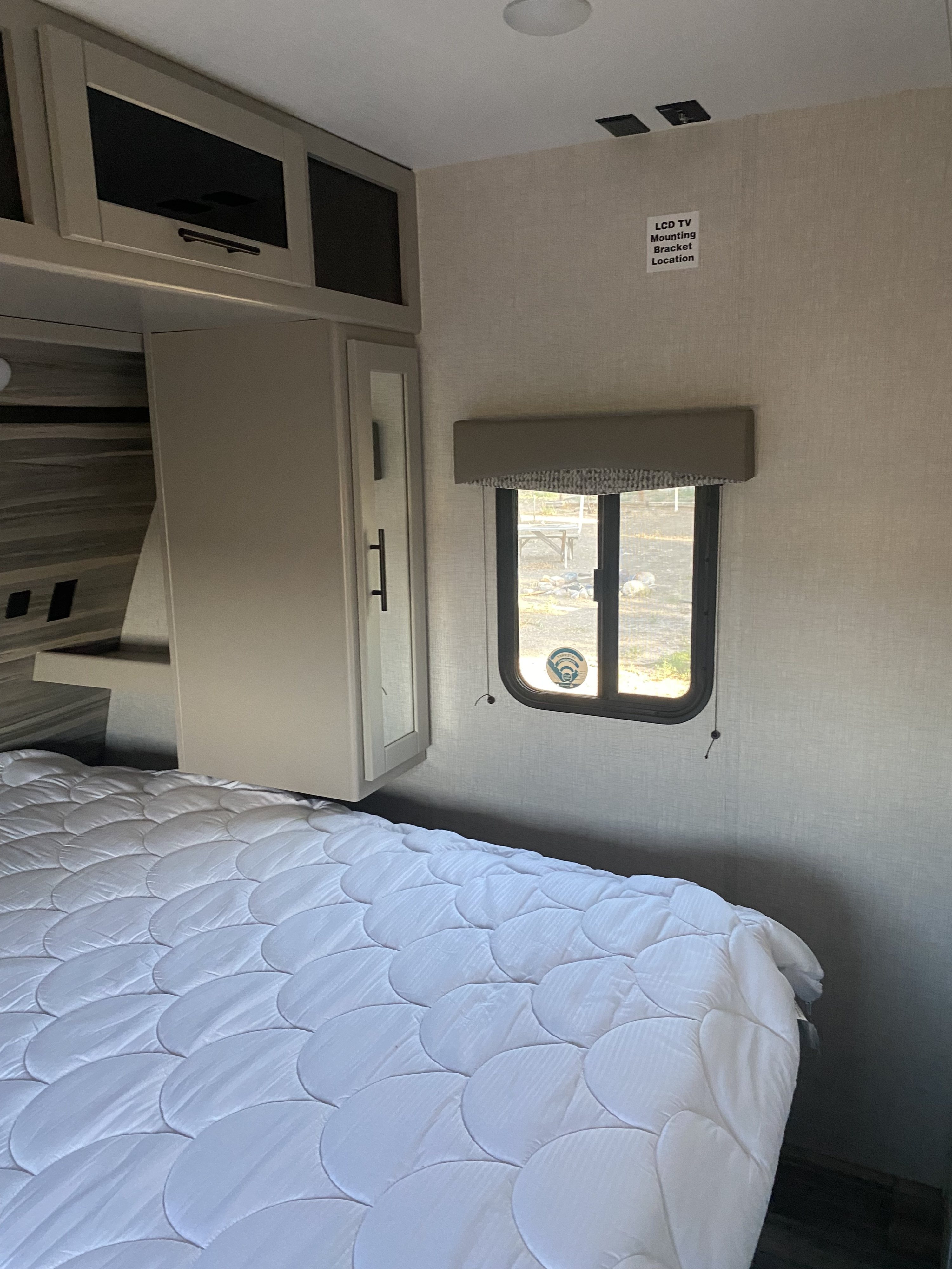 Cozy RV rental bedroom featuring a white quilted bed, overhead cabinets, window, and a designated TV mounting area.. Crossroads RV Cruiser Aire 2021