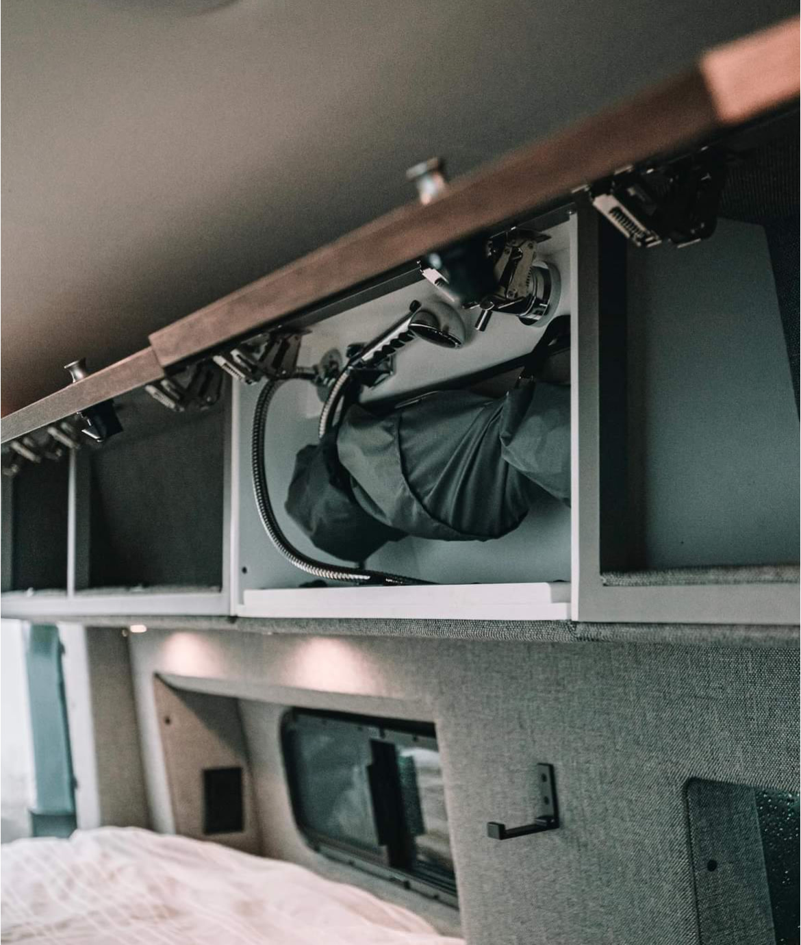 RV rental: Overhead cabinet reveals a compact stowed shower, hose, and storage, above a bed area.. Storyteller Overland Storyteller Overland Class B 2021
