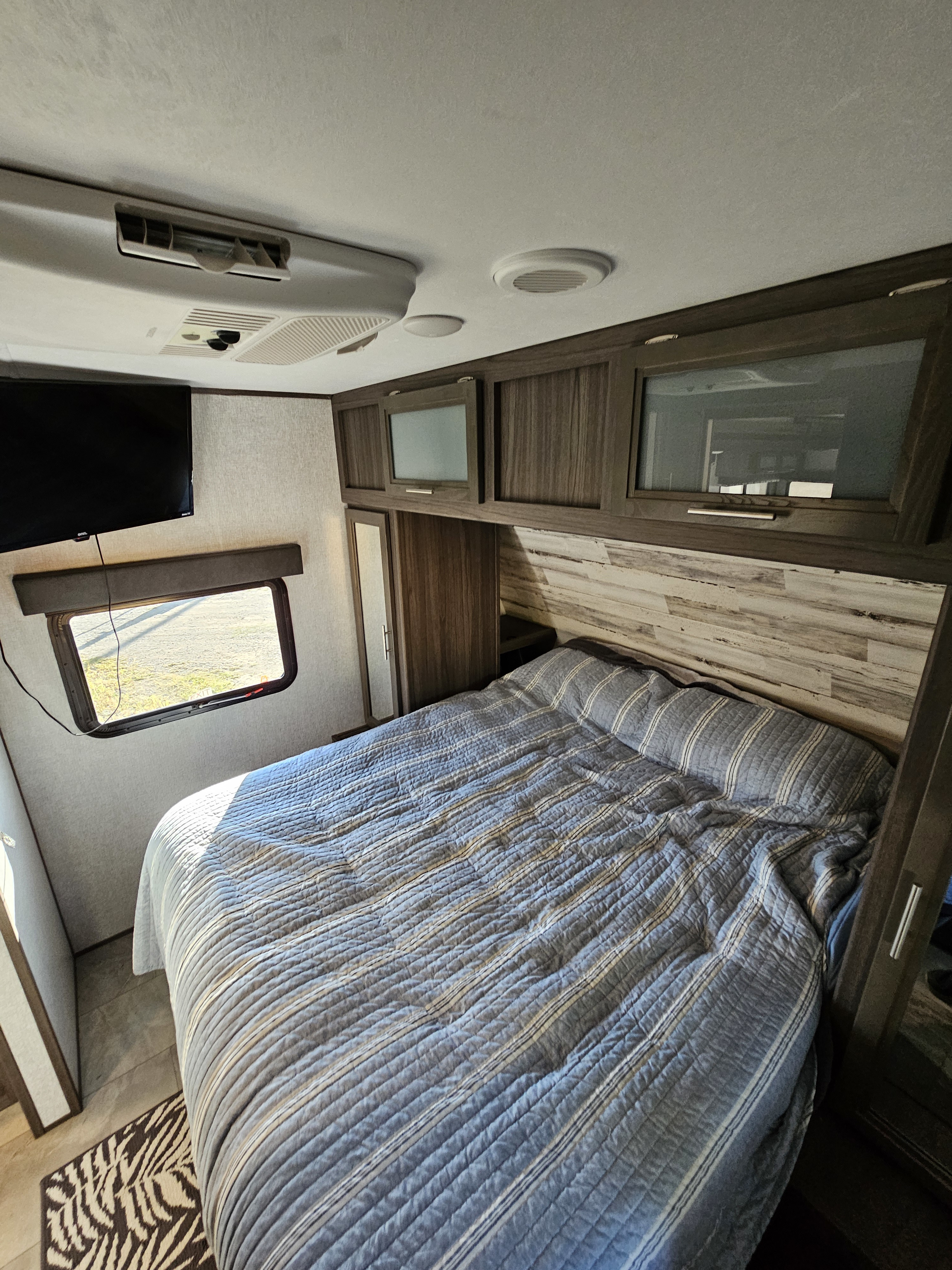 Cozy RV rental bedroom with a striped bed, mounted TV, overhead cabinets, and AC for a comfortable trip.. Dutchmen Kodiak Ultra Lite 2021
