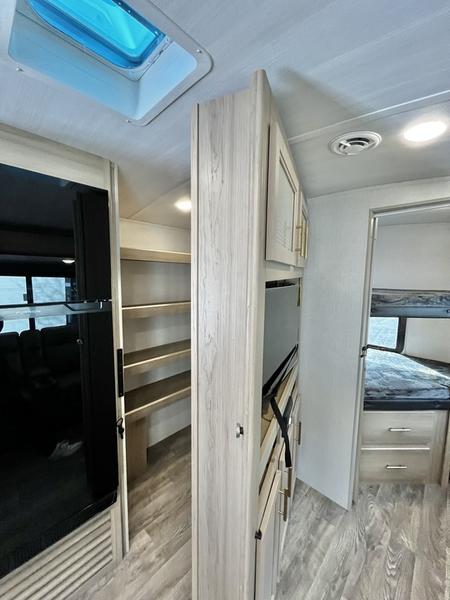 Inside a modern RV rental: skylight, wood-look cabinets, kitchen, pantry, and bunk beds in a light, clean style.. Keystone RV Outback Ultra Lite 2024