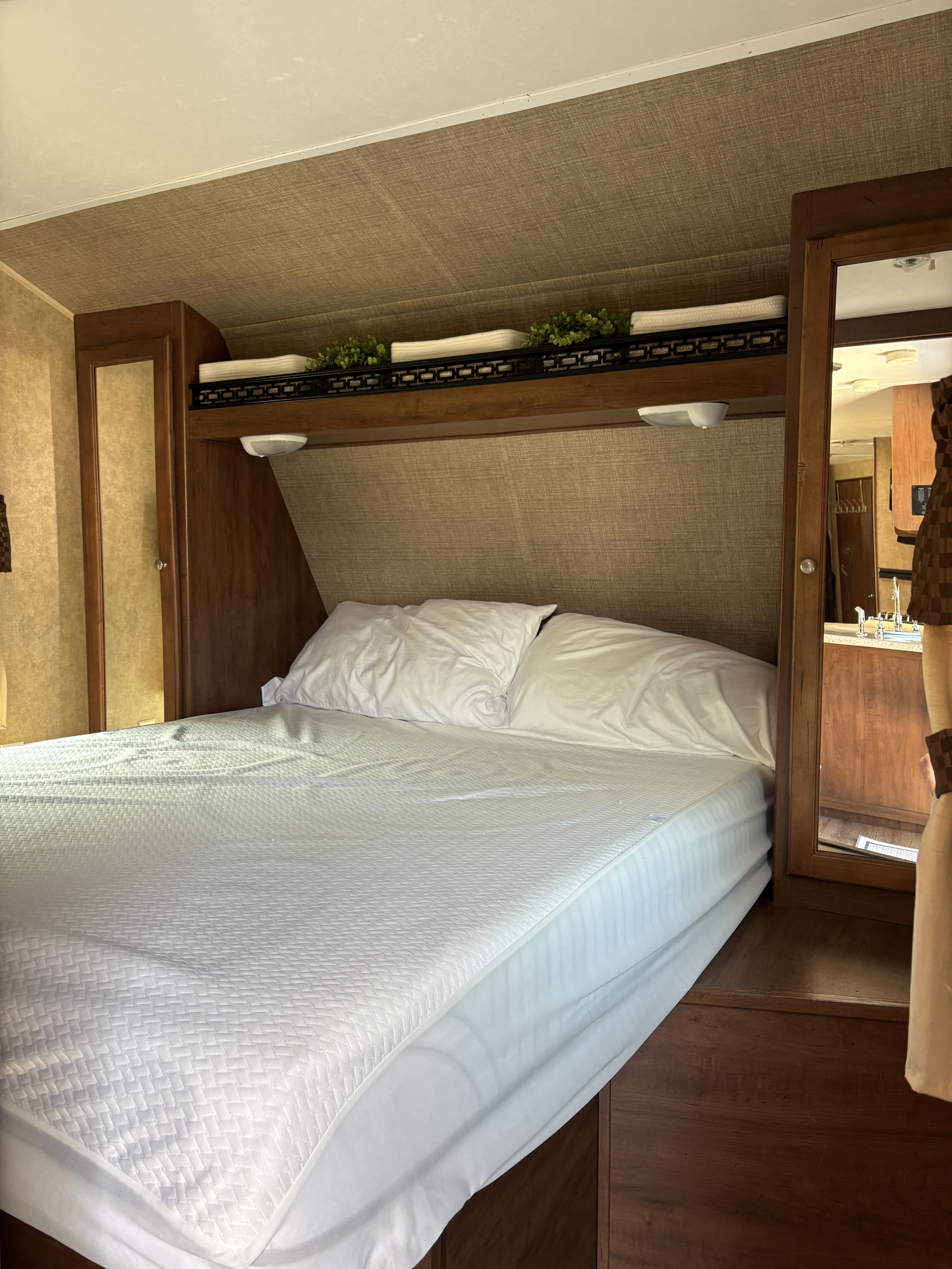 RV rental bedroom featuring a clean, white bed, overhead storage, and built-in mirrored closets.. Dutchmen Aspen Trail 2810BHS 2014