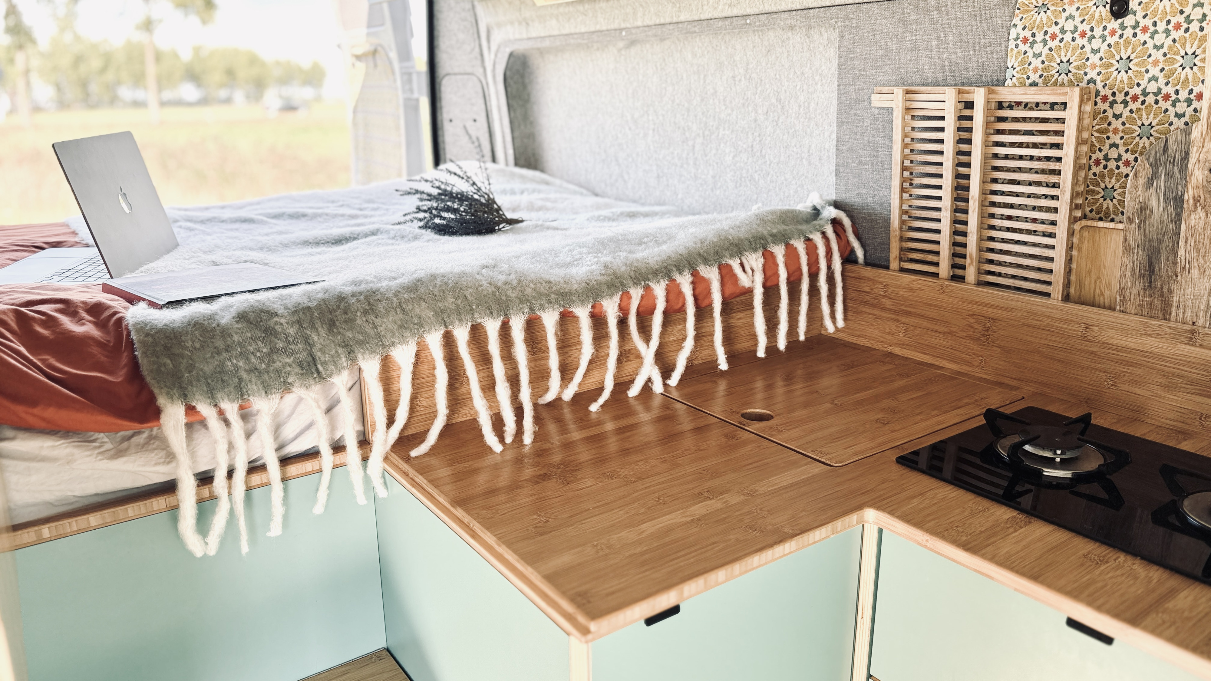 RV rental interior featuring a cozy bed with a laptop and a stylish kitchenette with a stovetop and bamboo countertop.. Fiat Ducato 2020