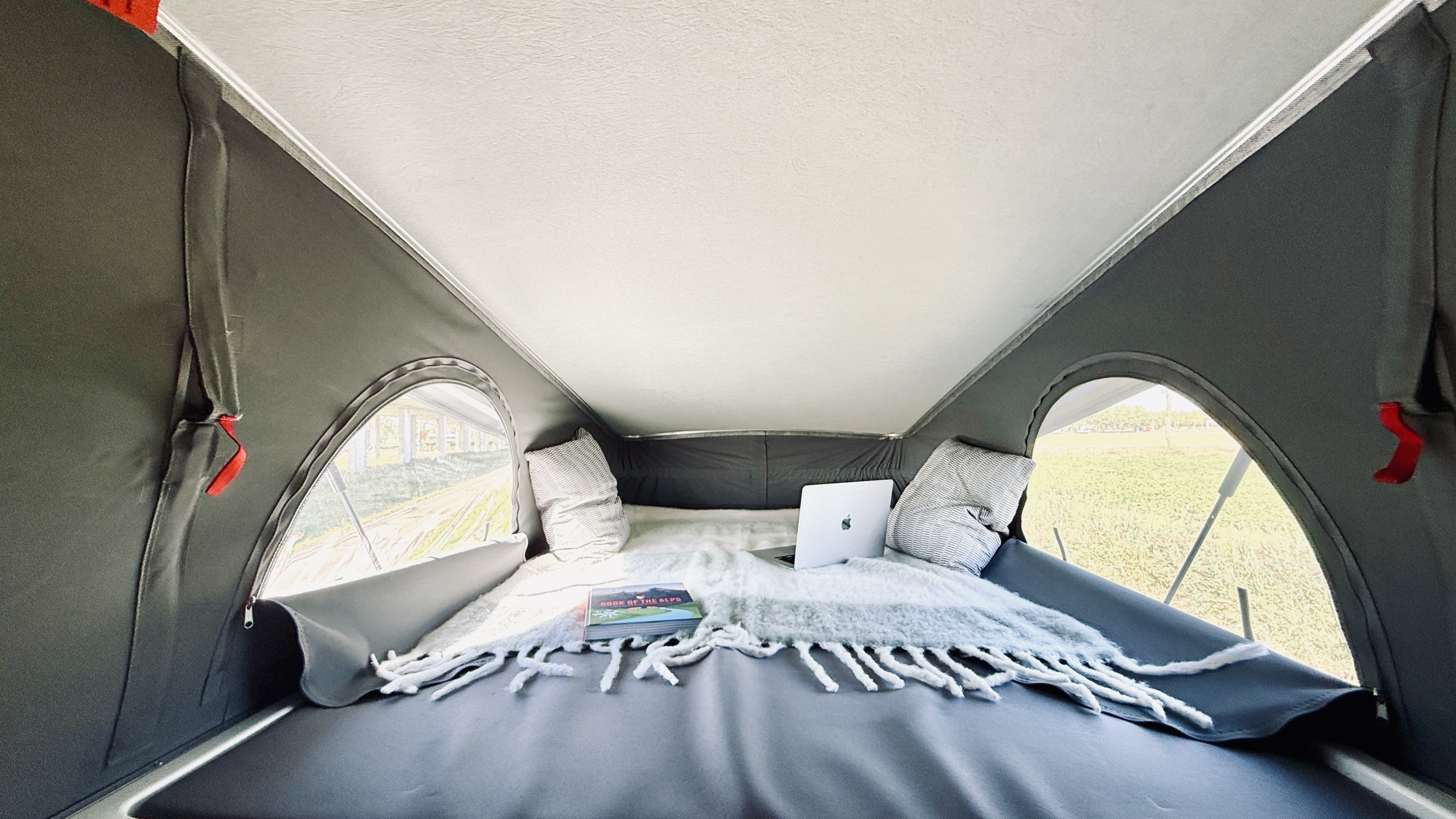 Cozy pop-top RV rental interior with a bed, laptop, and book, offering a comfy mobile workspace with scenic views.. Fiat Ducato 2020