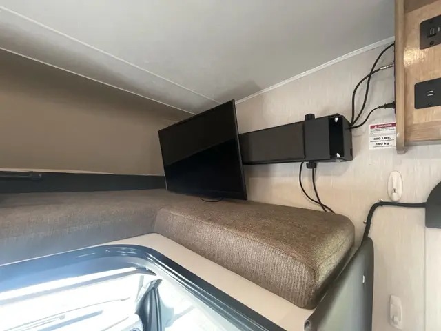 RV rental interior: A TV on an extendable mount is positioned above the cozy cab-over bunk, complete with cushions & power access.. Forest River Coachmen Leprechaun 2021