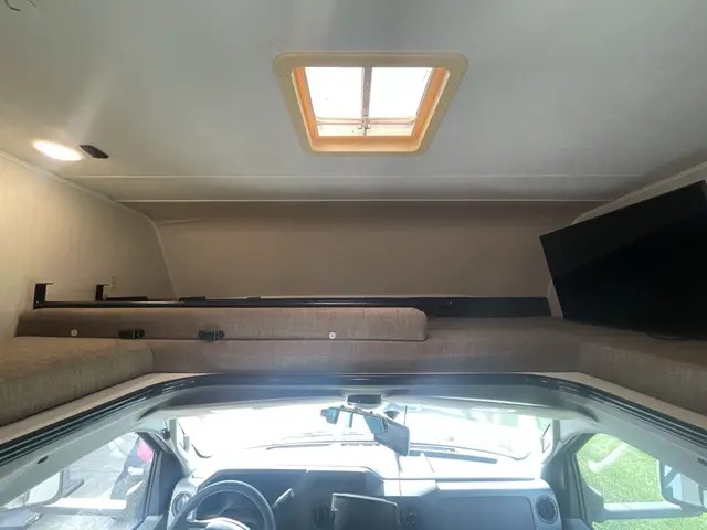 This RV rental interior shows a cozy cab-over bed, overhead skylight, and TV, offering a comfortable space above the driver's cab.. Forest River Coachmen Leprechaun 2021