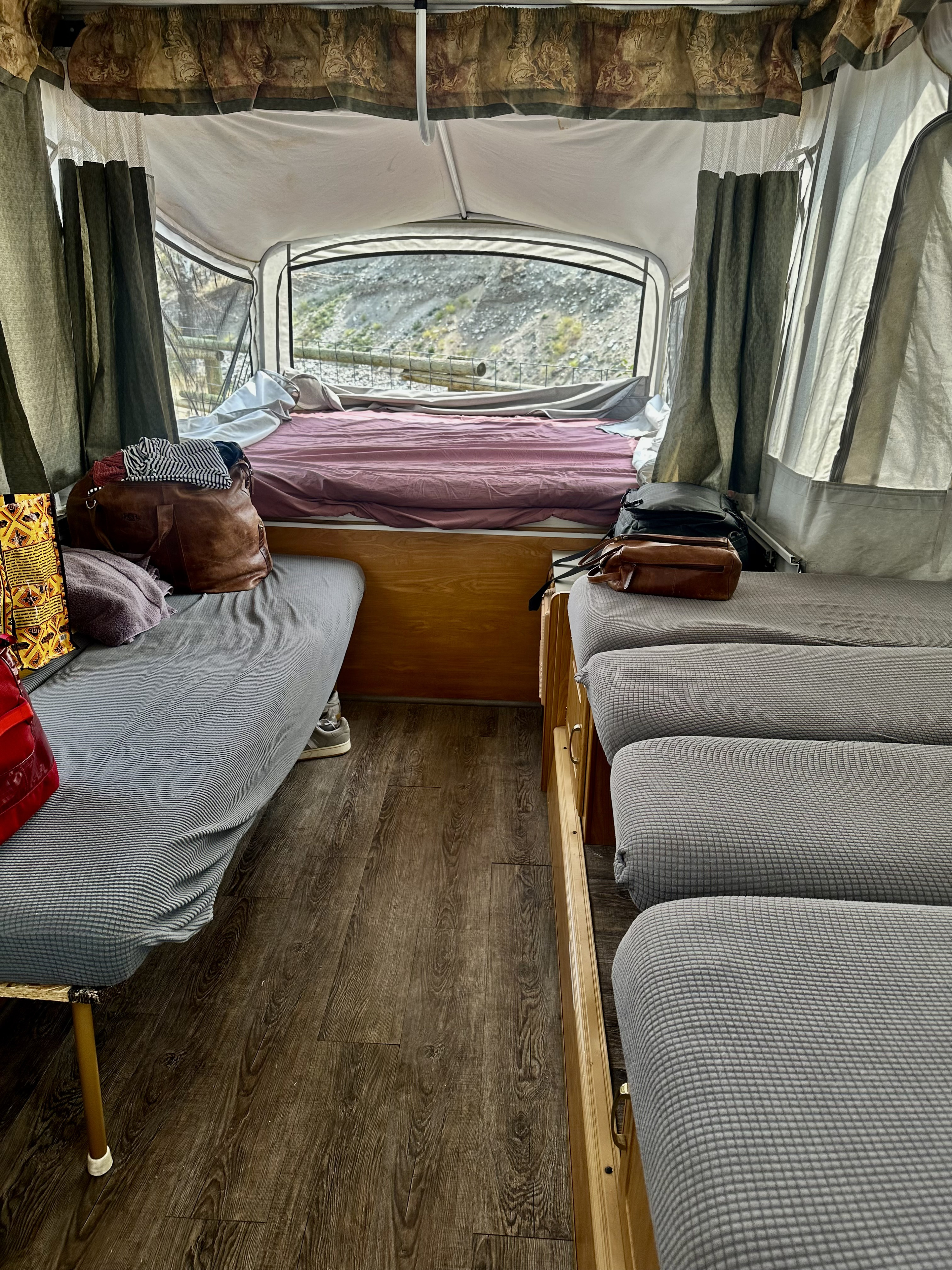 Cozy RV rental interior with beds, seating, and scenic mountain views through the rear window.. Coleman Americana Utah 2004