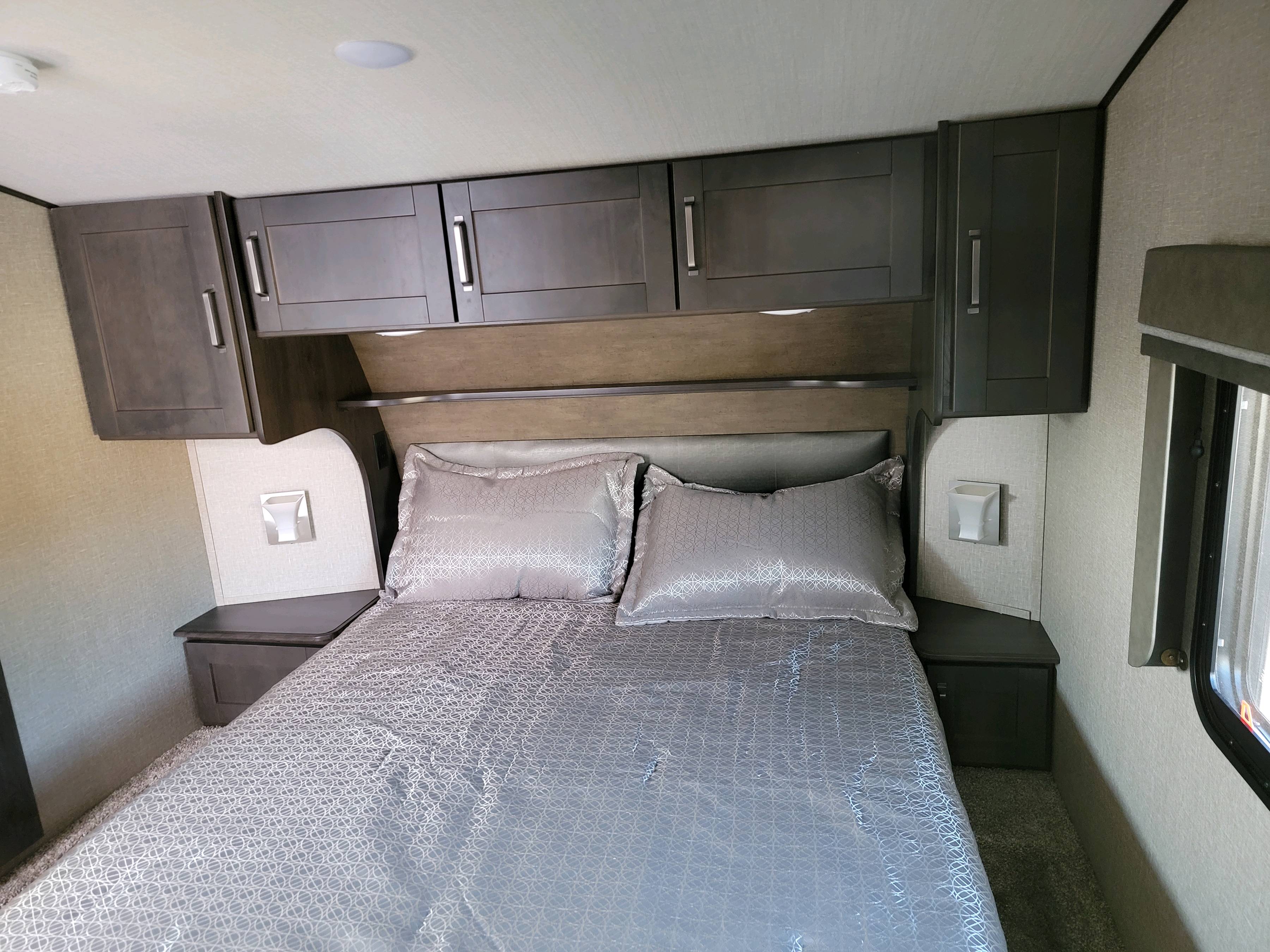 RV rental bedroom with a cozy bed, grey patterned linens, overhead cabinets, and side tables.. Grand Design Reflection 2022