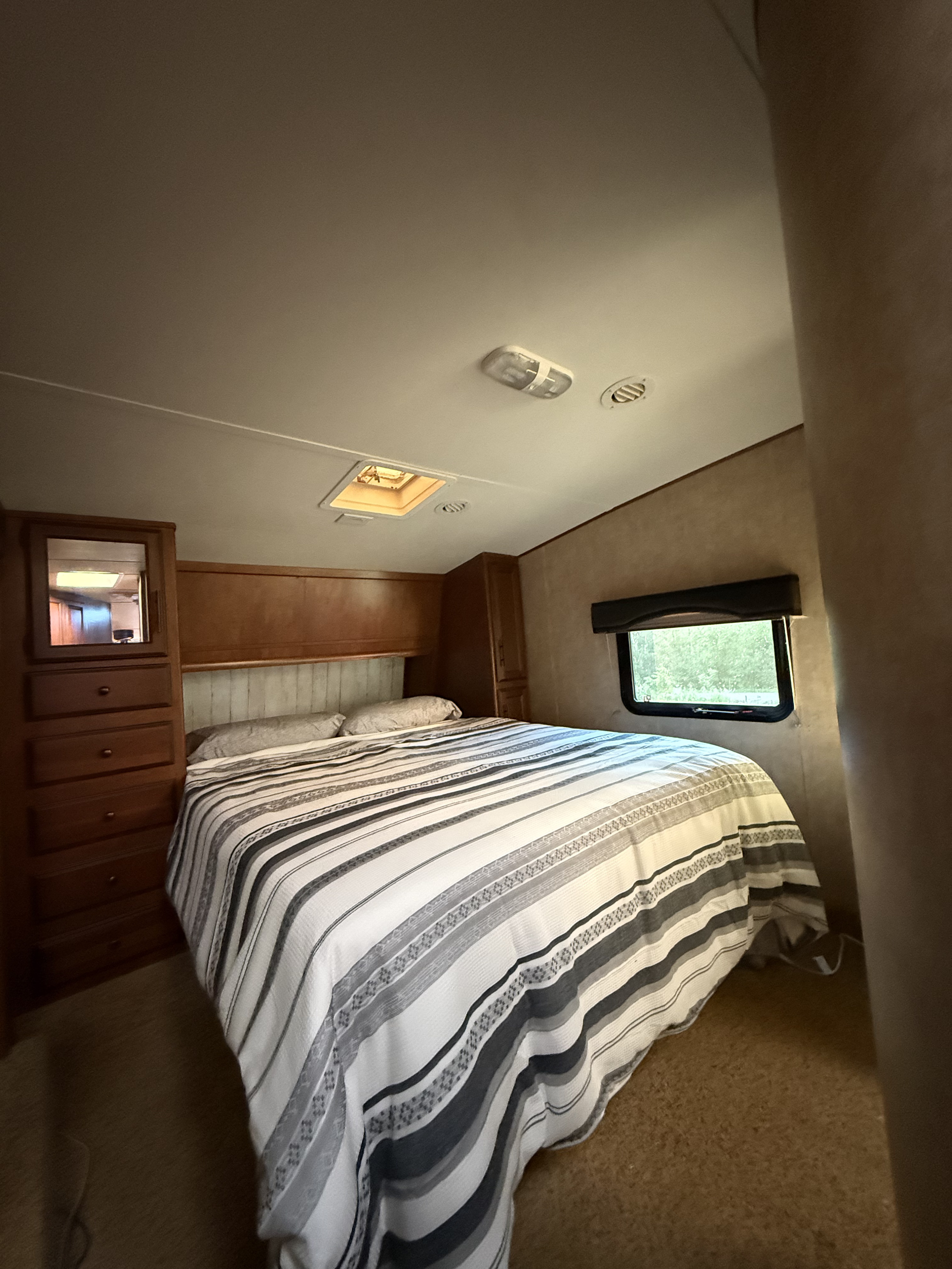 Inside an RV rental: a cozy bedroom with a striped bed, built-in dresser, and a window to nature.. Raven Raven Fifth Wheel 2012