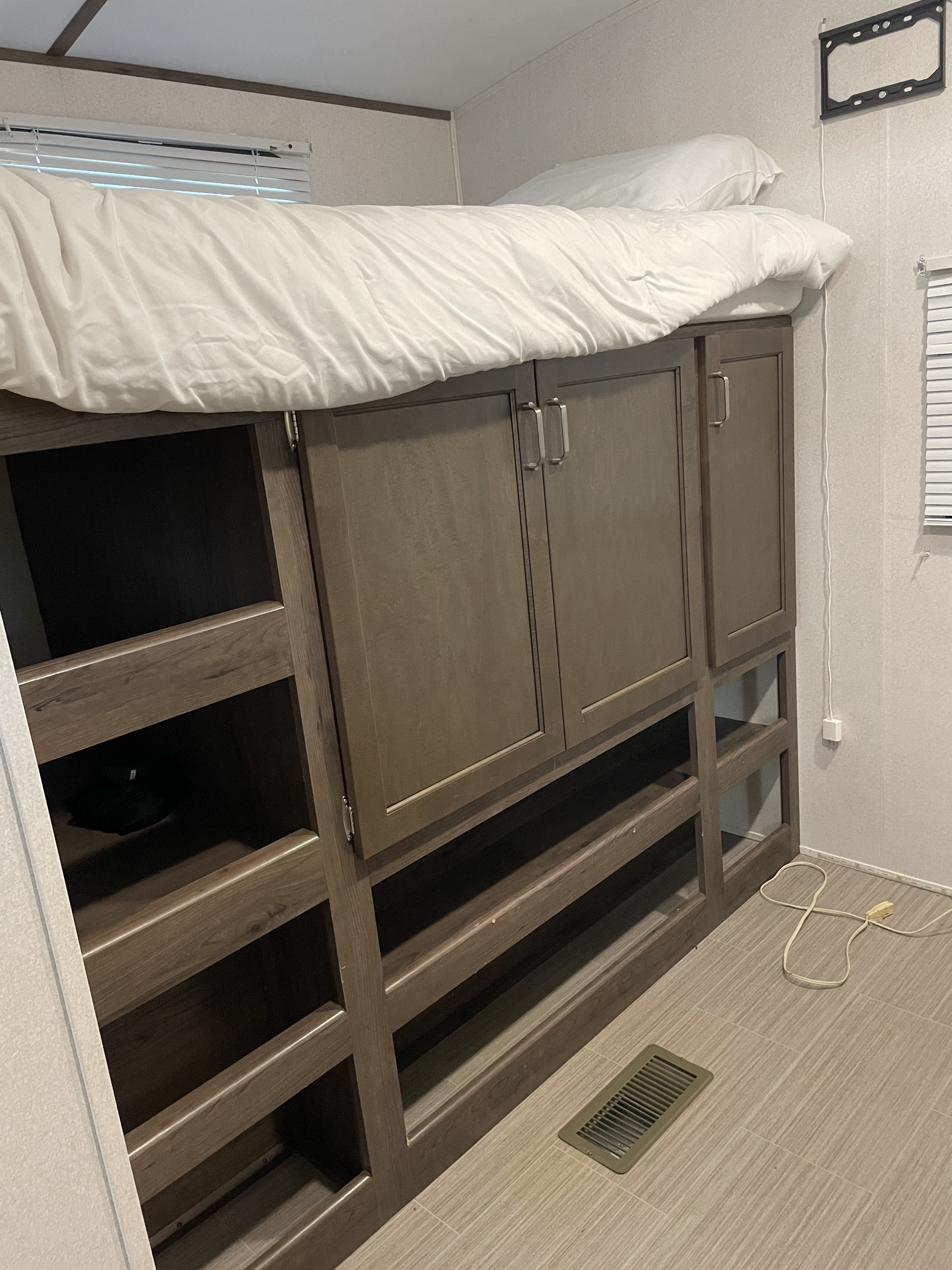 Interior view of an RV rental showing a top bunk bed with white bedding, integrated wooden cabinets, and shelving.. Keystone RV Passport Grand Touring 2020