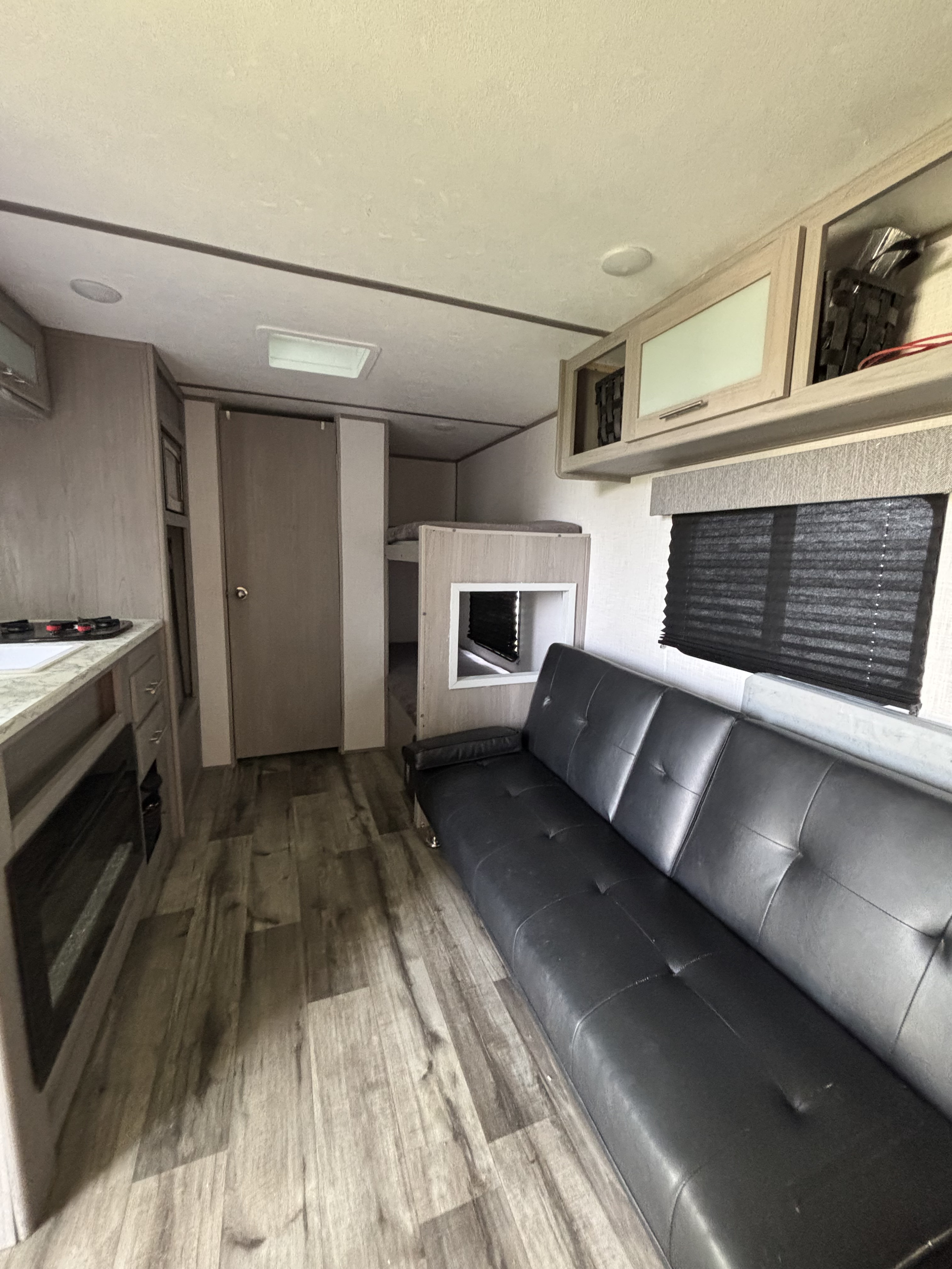 Bright RV rental interior showing a compact kitchen area, bunk beds, a black sofa, and ample overhead storage.. Dutchmen Coleman Lantern LT 2022