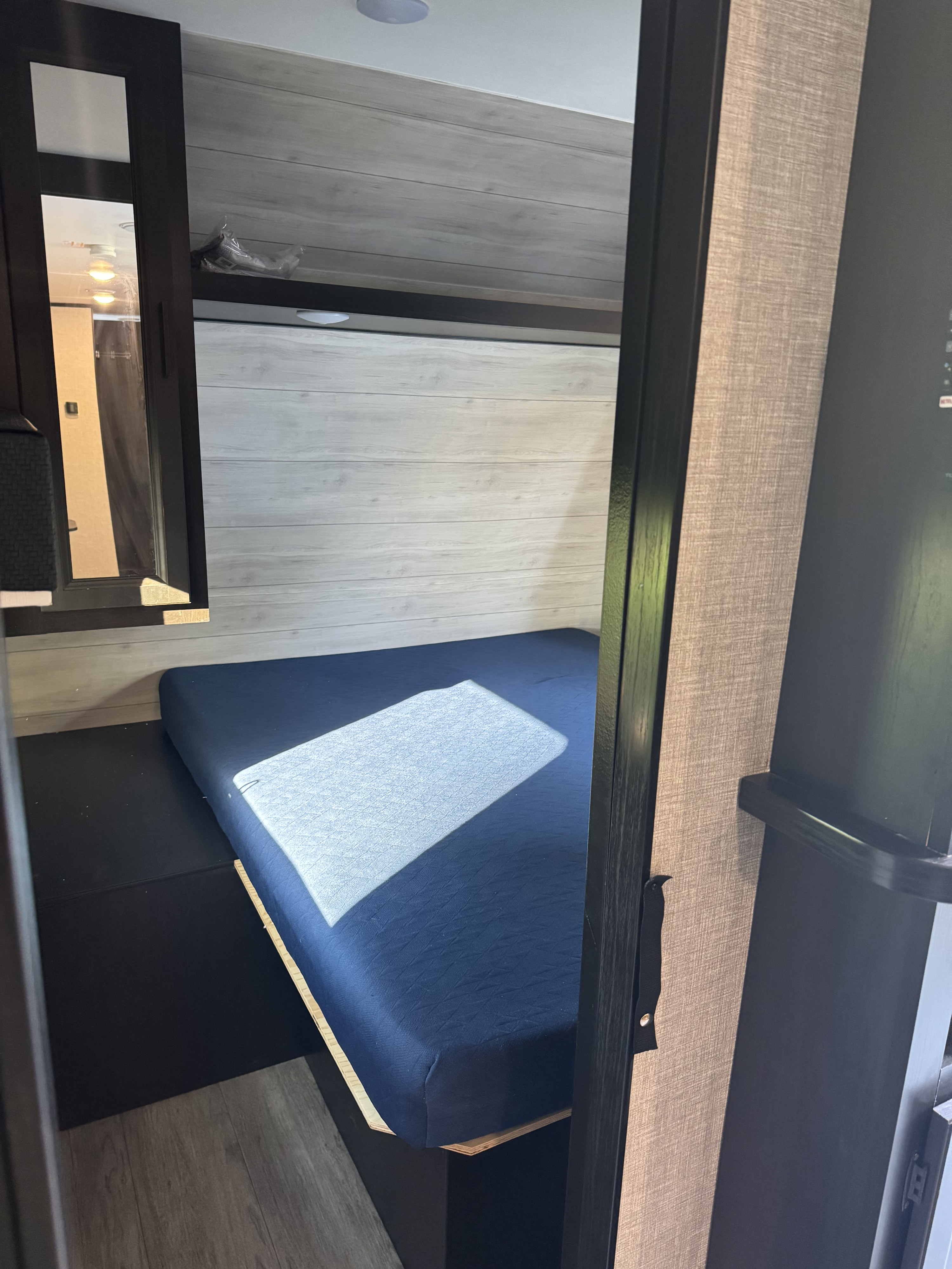 An RV rental's cozy bunk bed nook with light wood paneling & a blue mattress. Sunlight creates a bright rectangle on the bed.. Jayco Jay Flight SLX 2022