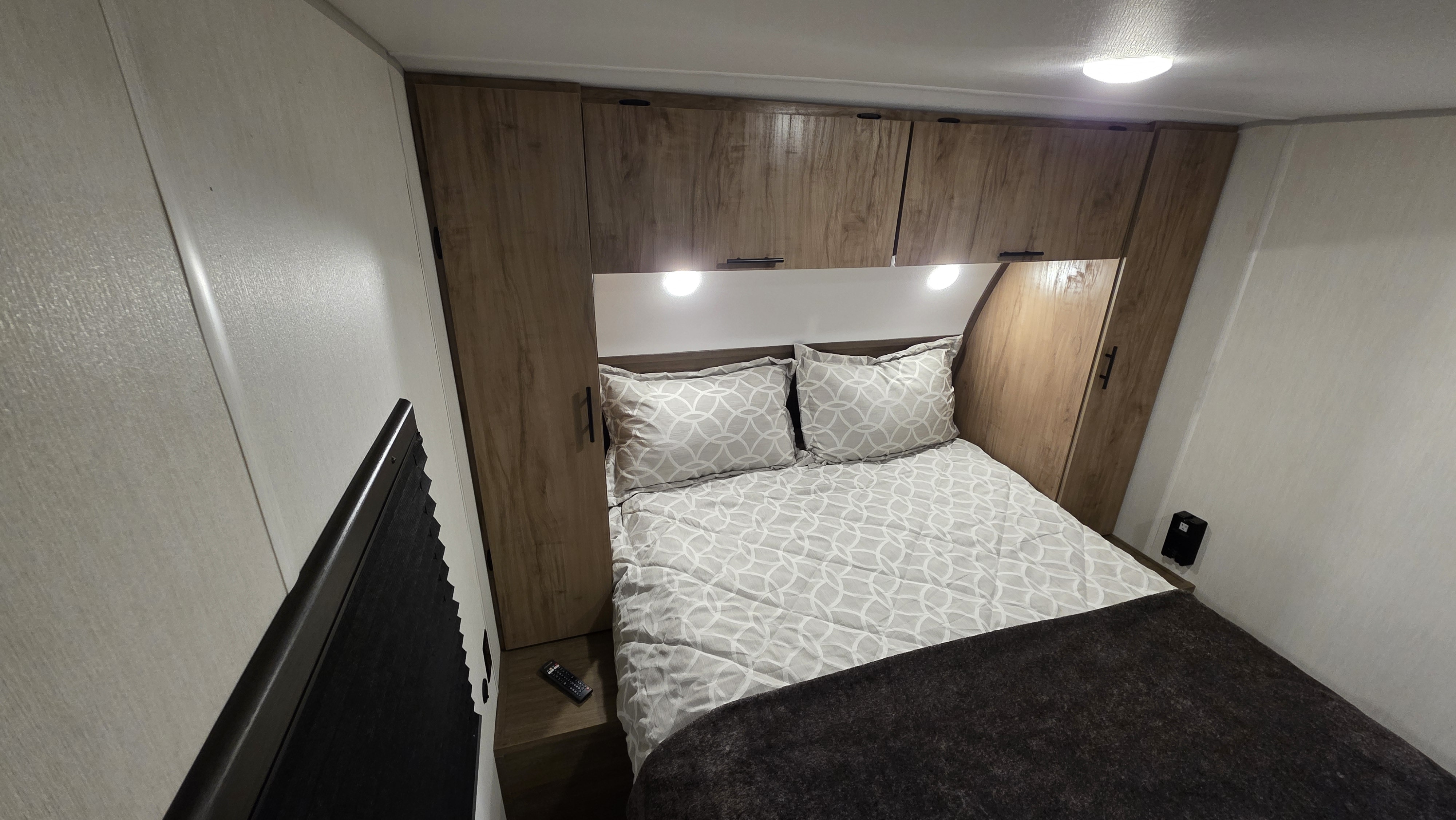 Cozy RV rental bedroom featuring wood cabinets, soft lighting, patterned bedding, and a black window blind.. Forest River Cherokee Grey Wolf 2025