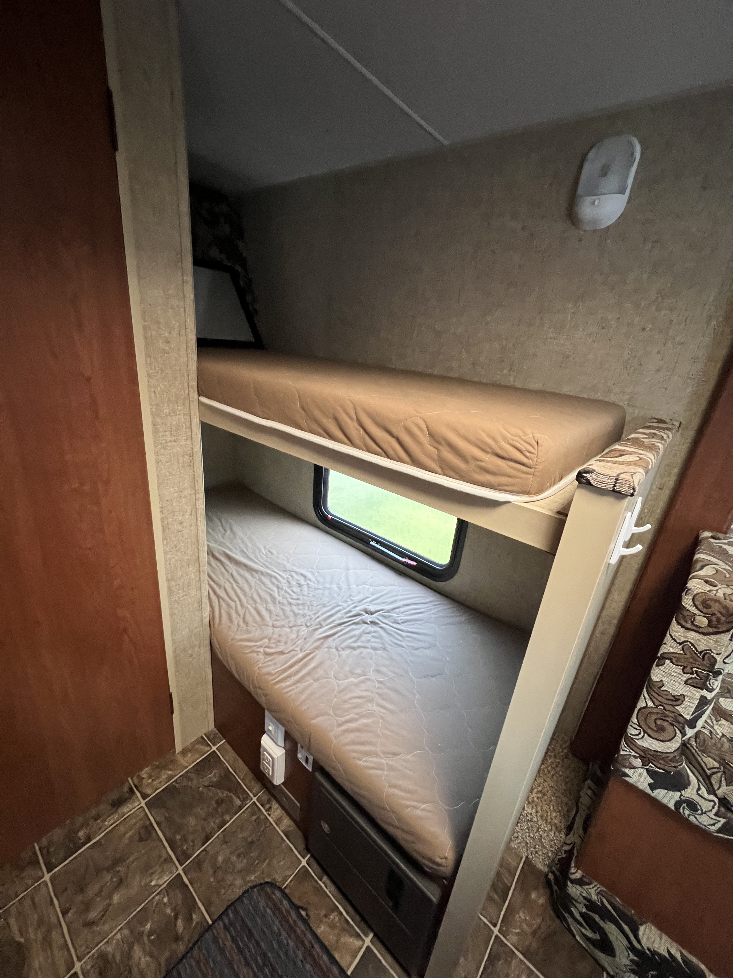 RV rental interior with cozy bunk beds. Upper bunk, lower bunk with window, wall light, and patterned seating offer comfort.. Sportsmen Classic 2014