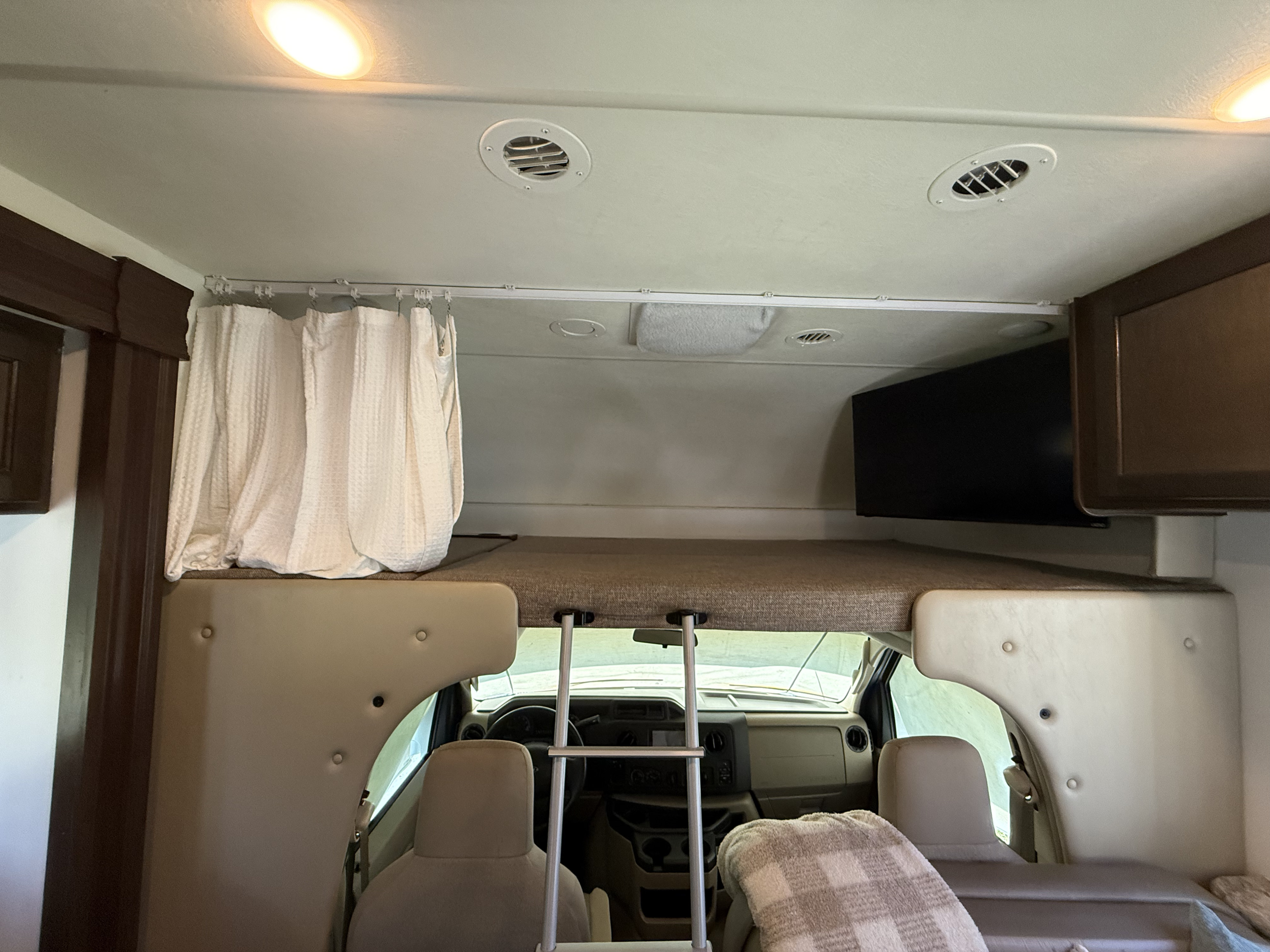 RV rental interior: Features an over-cab bunk bed with privacy curtain, ladder, and a TV above the cockpit area.. Thor Freedom Elite 2018