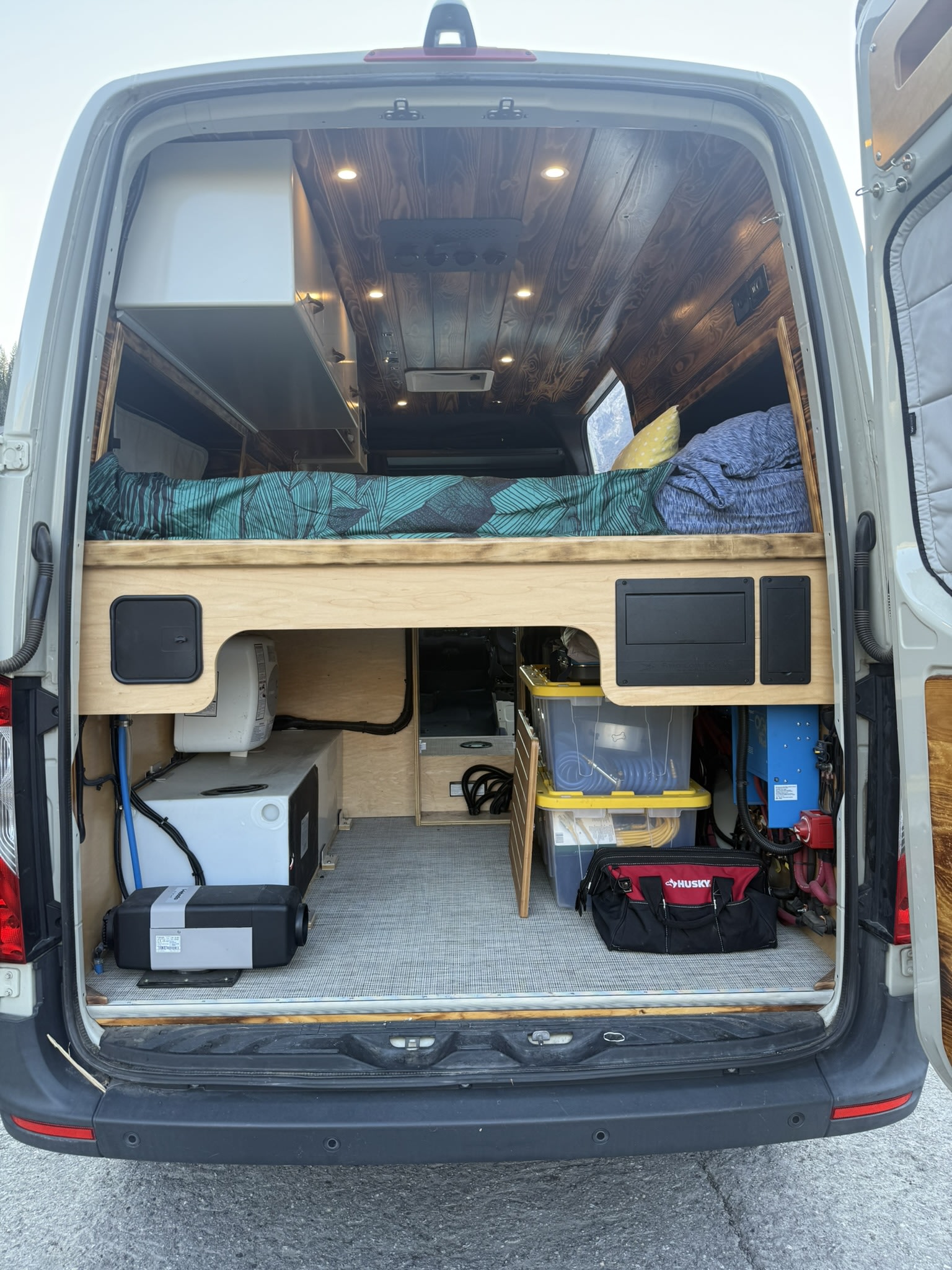 Inside an rv rental camper van: elevated bed, under-bed storage with water tank, heater, and electrical systems.. Mercedes-Benz Sprinter 2019