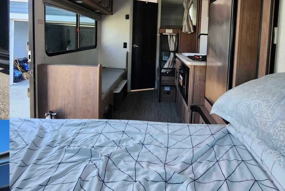 Inside an RV rental, showing bunk beds, a kitchen with microwave, and a cozy foreground bed for travelers.. Forest River No Boundaries 16 6 2023