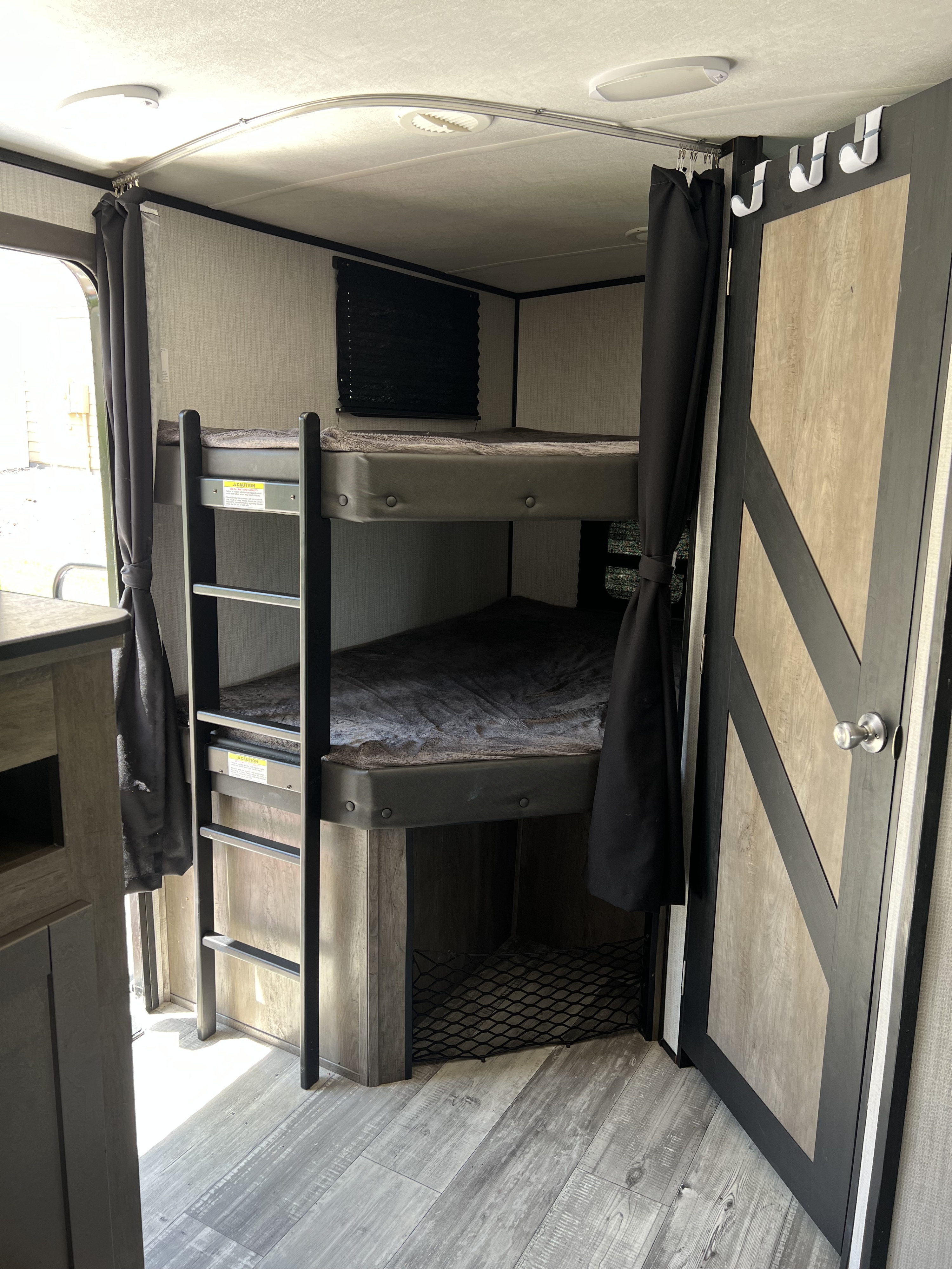 RV rental's cozy bunk beds, featuring a ladder, privacy curtains, and a light-toned interior.. Heartland RVs North Trail 2021