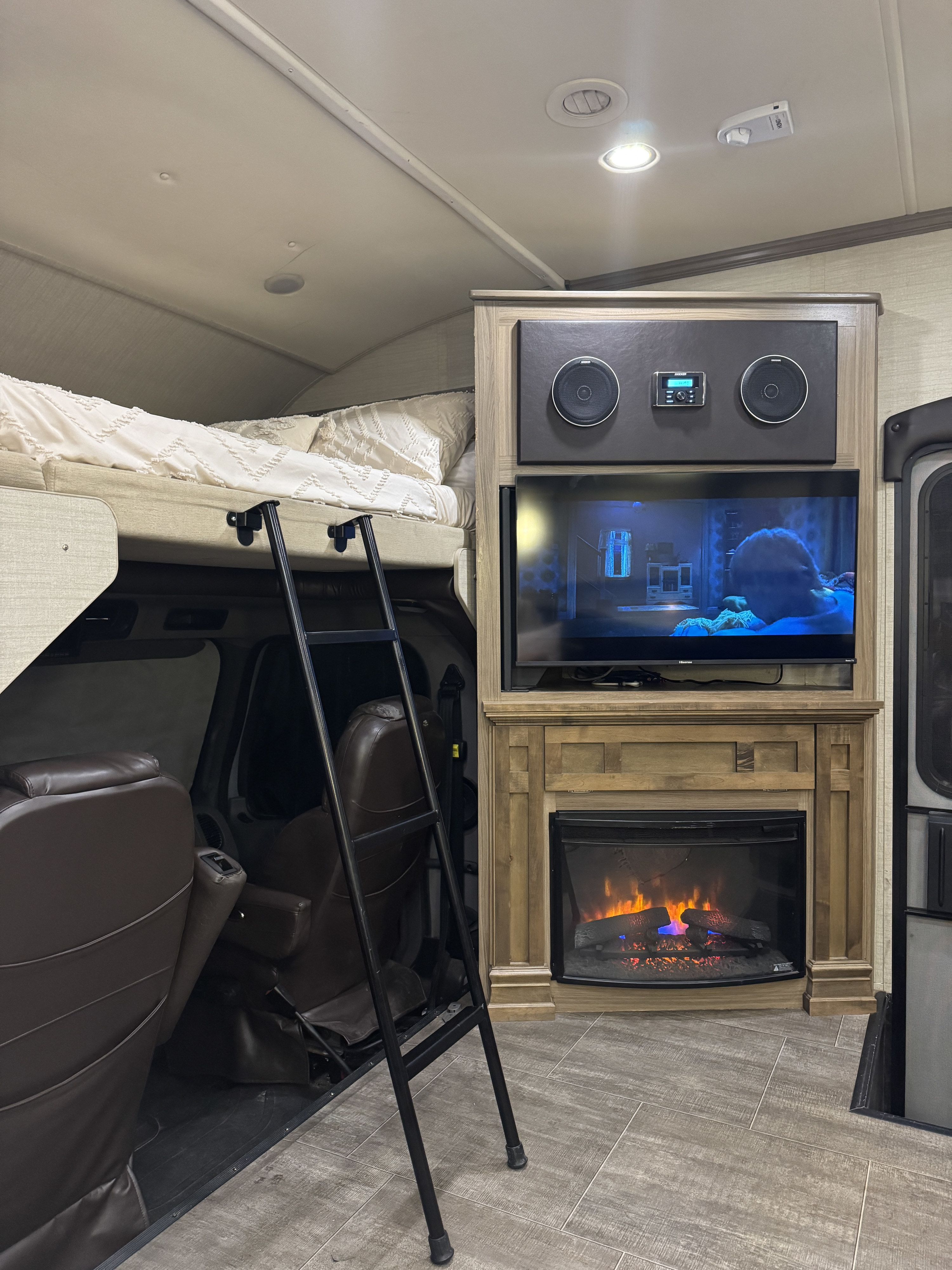 Cozy RV rental interior with over-cab bed, ladder, TV, and electric fireplace. Ideal for compact living.. Jayco Seneca 2018