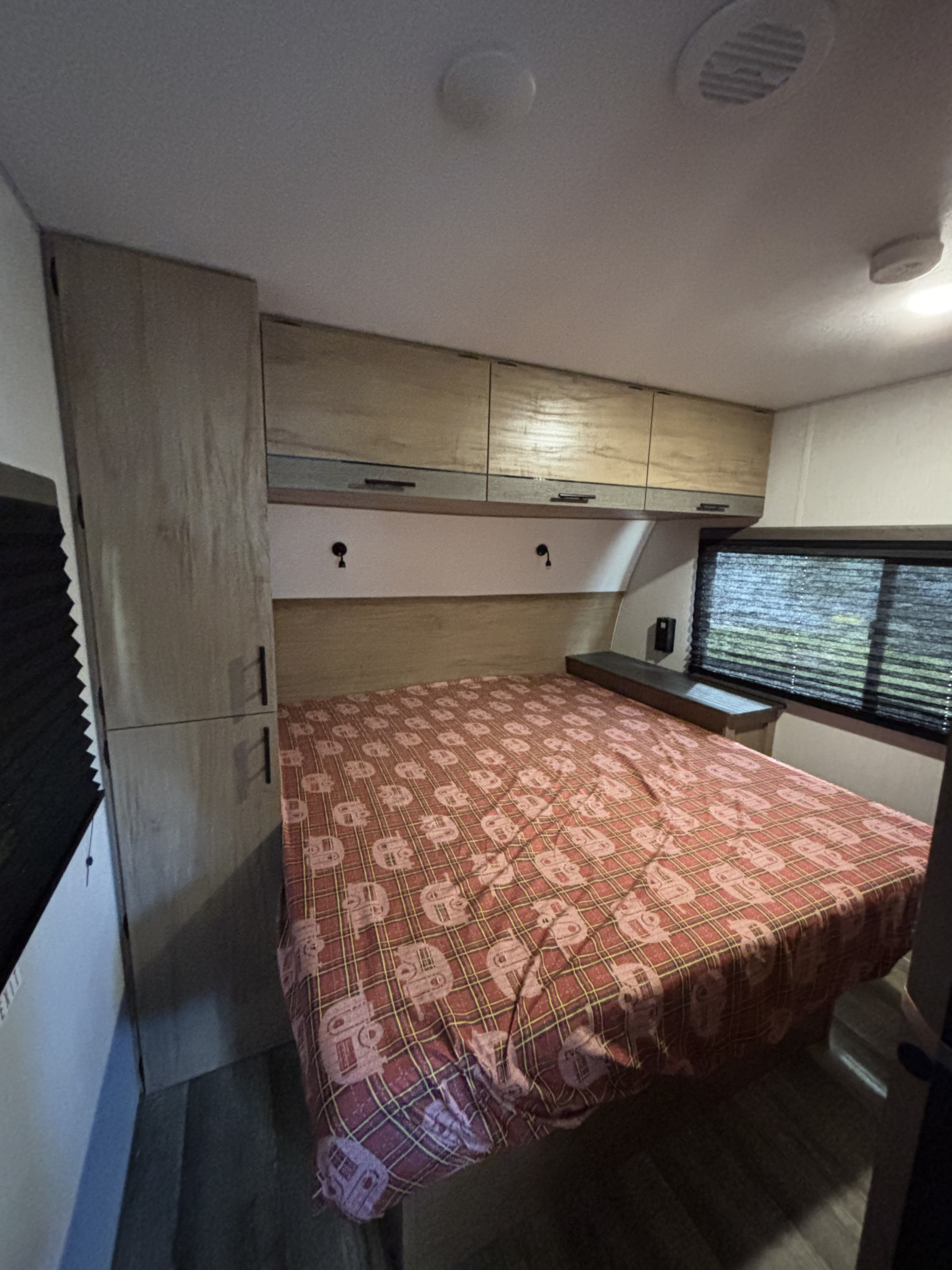 Explore this cozy RV rental bedroom. Features include a comfy bed with unique camper bedding, overhead cabinets, and a window.. Forest River Campsite Reserve 23LM 2024