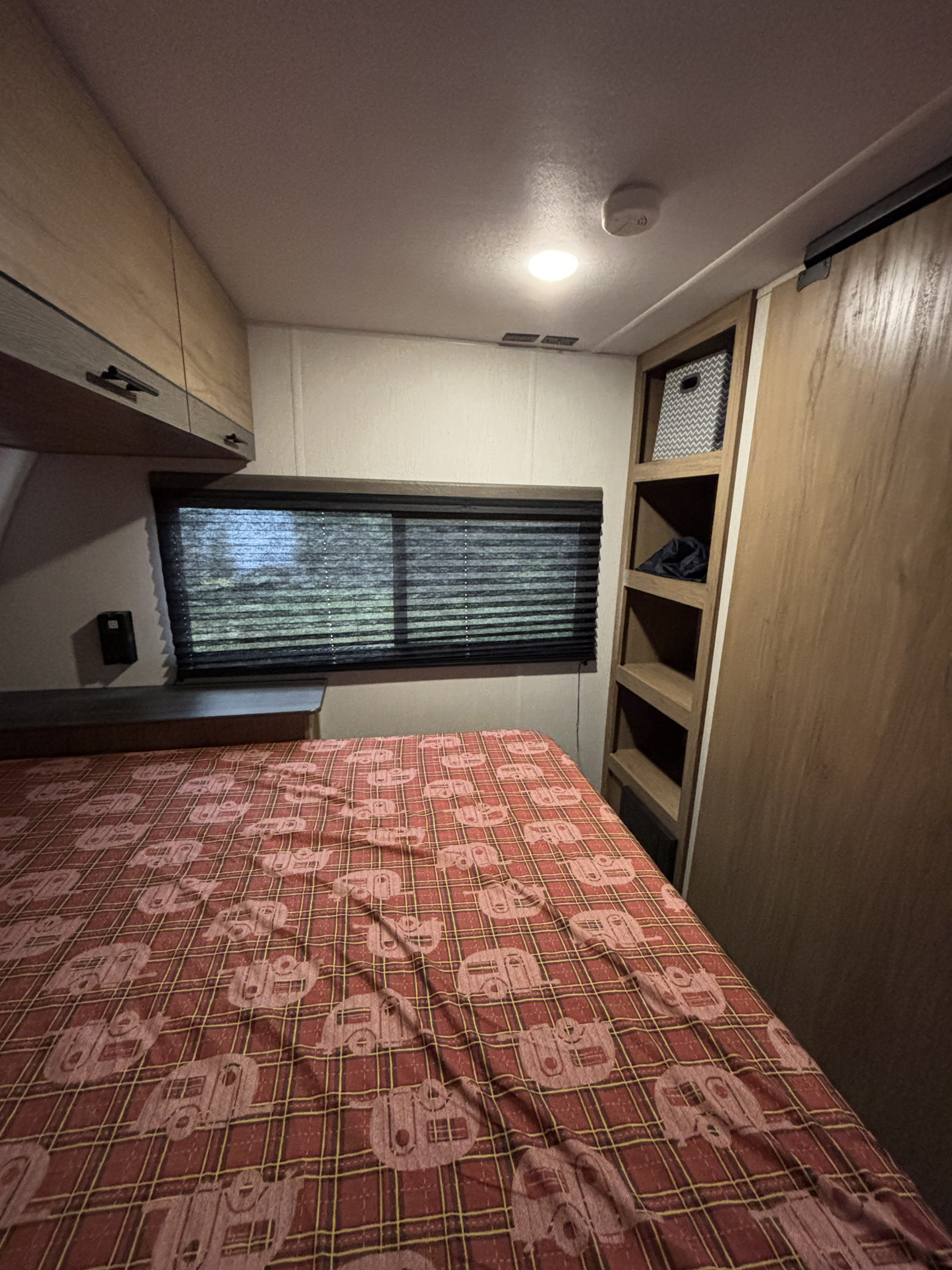 Cozy RV rental bedroom with plaid bedding featuring camper motifs, window, and built-in storage.. Forest River Campsite Reserve 23LM 2024