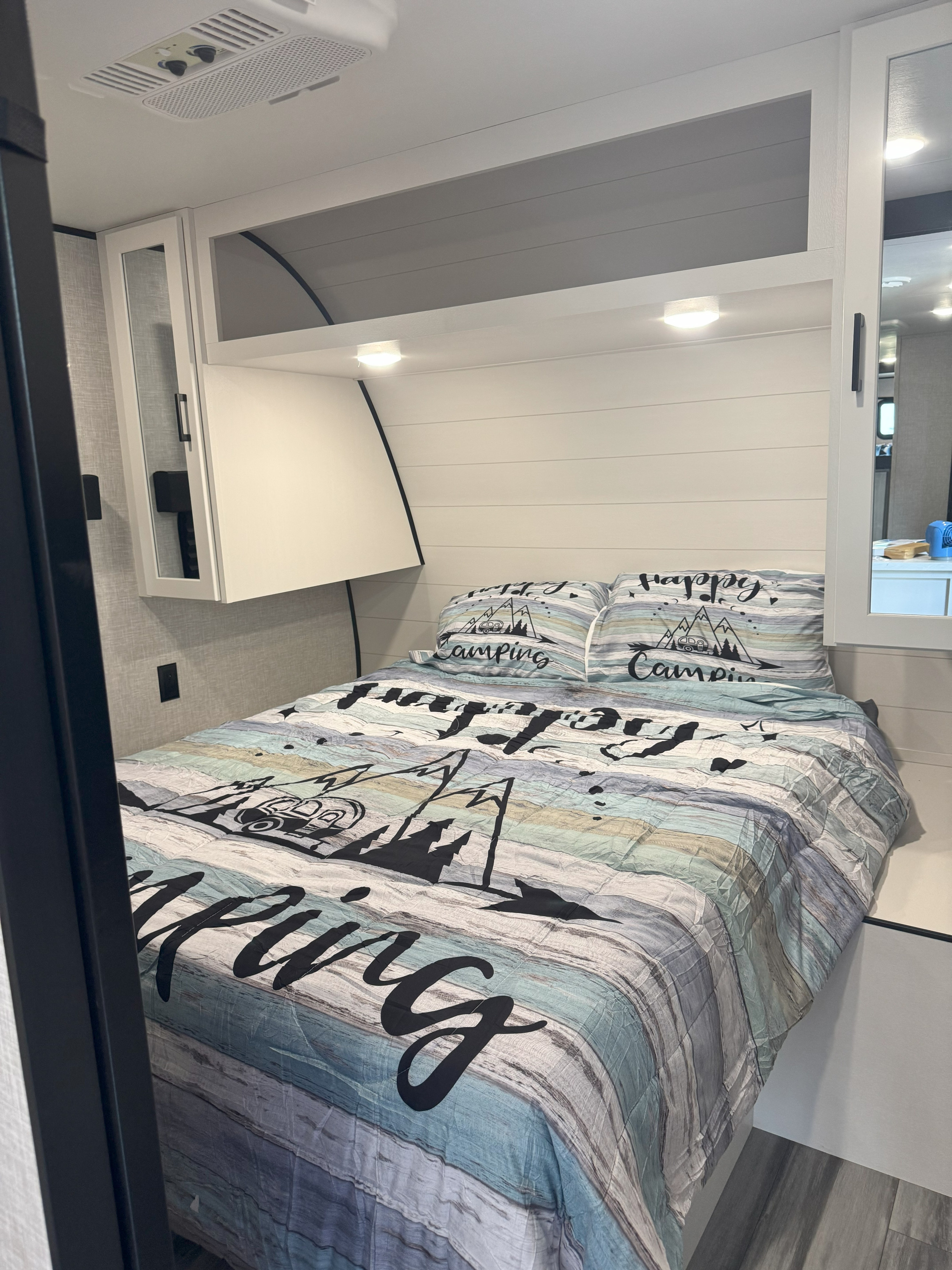 Cozy rv rental bedroom: A bed with "Happy Camping" bedding, shiplap wall, overhead storage, and AC unit. Ideal for travel!. Jayco Jay Jay Flight 294QBS 2025