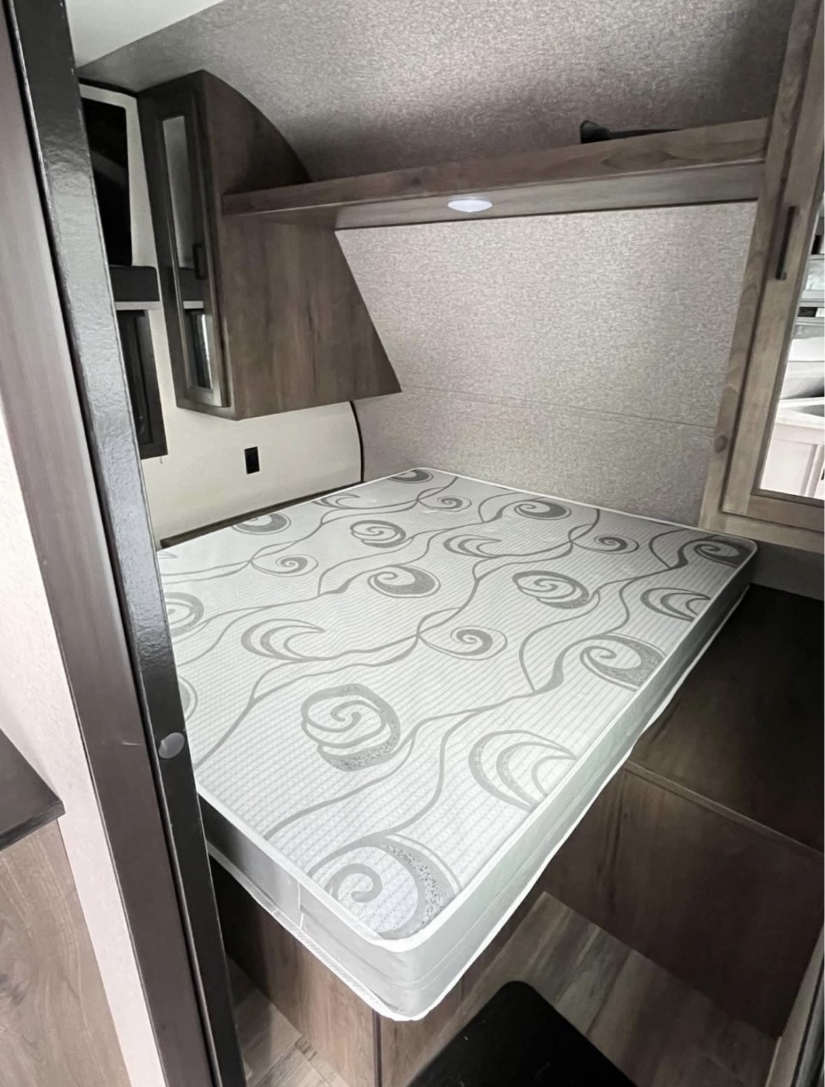RV rental sleeping area with a patterned mattress, wooden overhead storage, and integrated lighting. Cozy and compact for travel.. Highland Ridge RV Open Range 2022