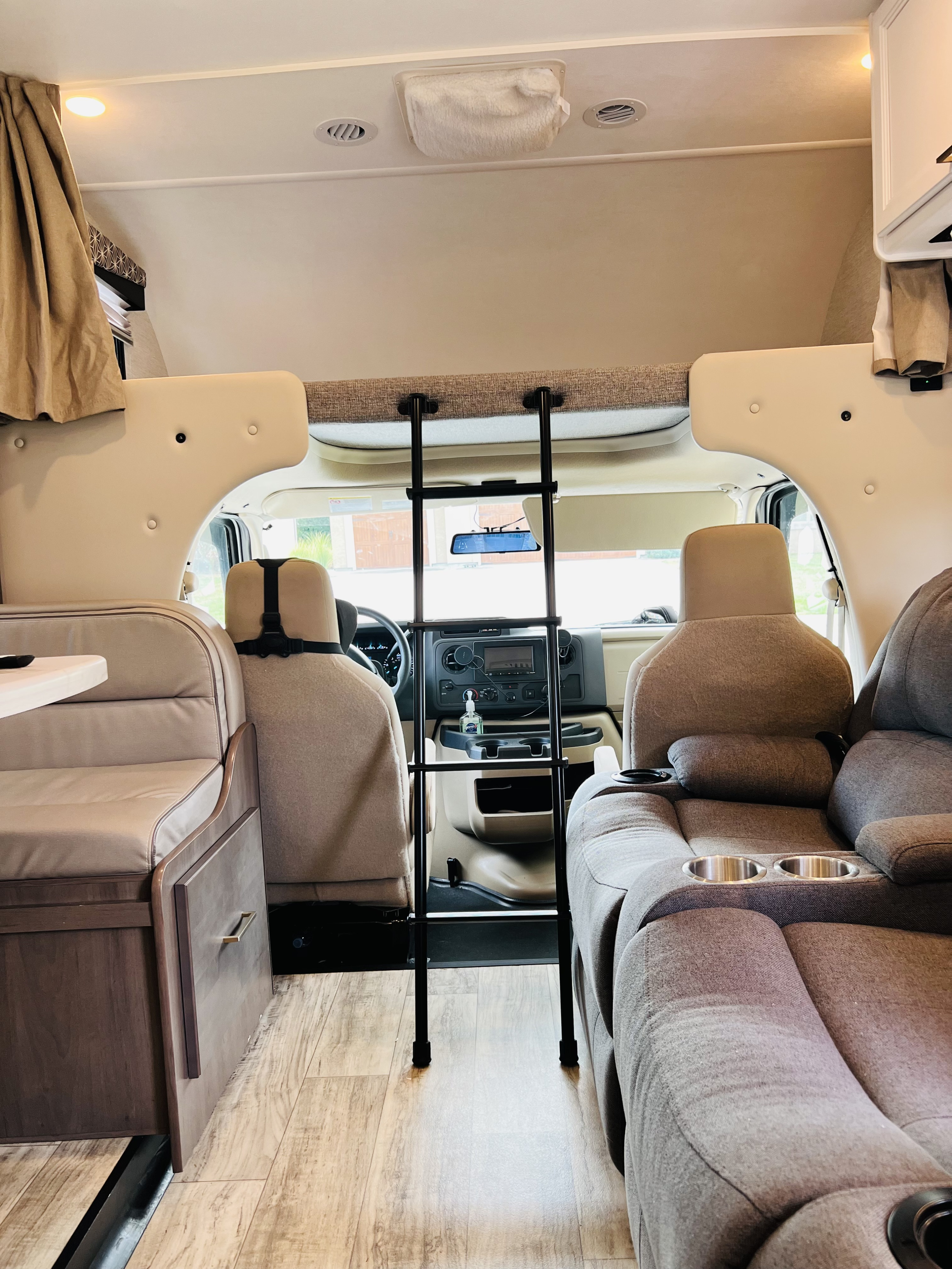 Inside an RV rental: view of the cab, overhead bunk bed with ladder, dinette, and cozy recliner seats.. Thor Freedom Elite 2024
