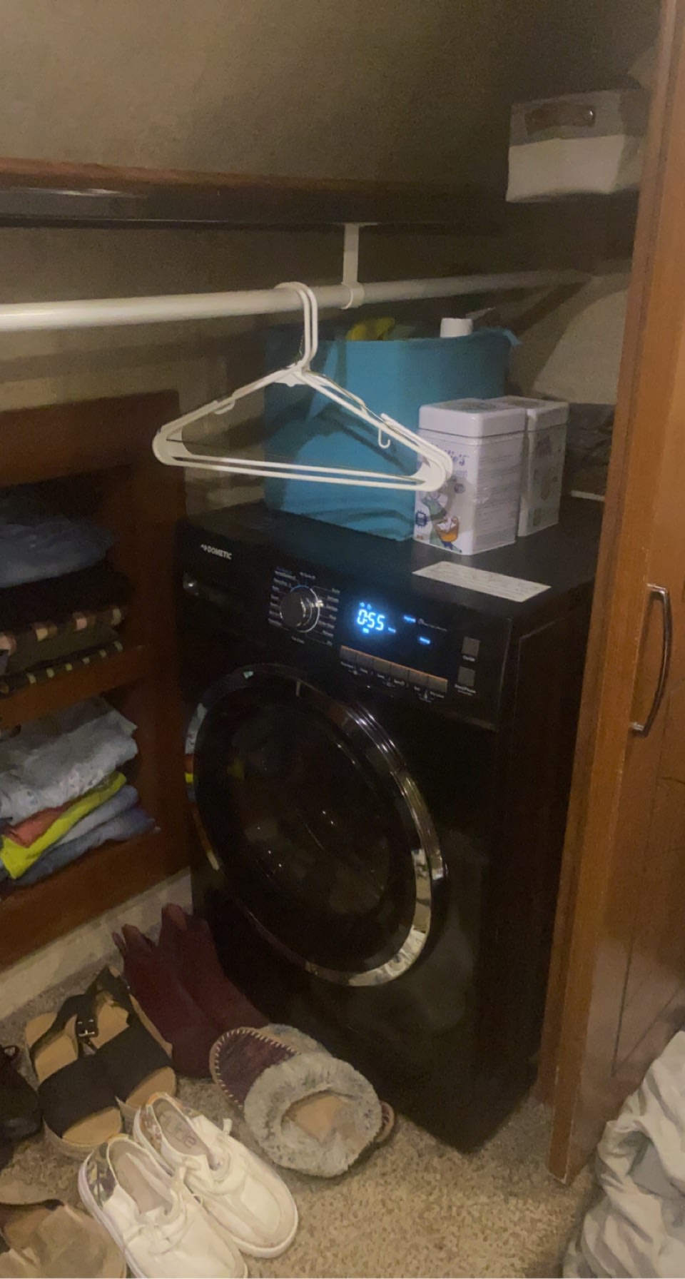 Inside an RV rental: a running Dometic washing machine (0:55 remaining), shelves with clothes, and shoes on the floor. Compact laundry area.. Forest River Sierra 2016