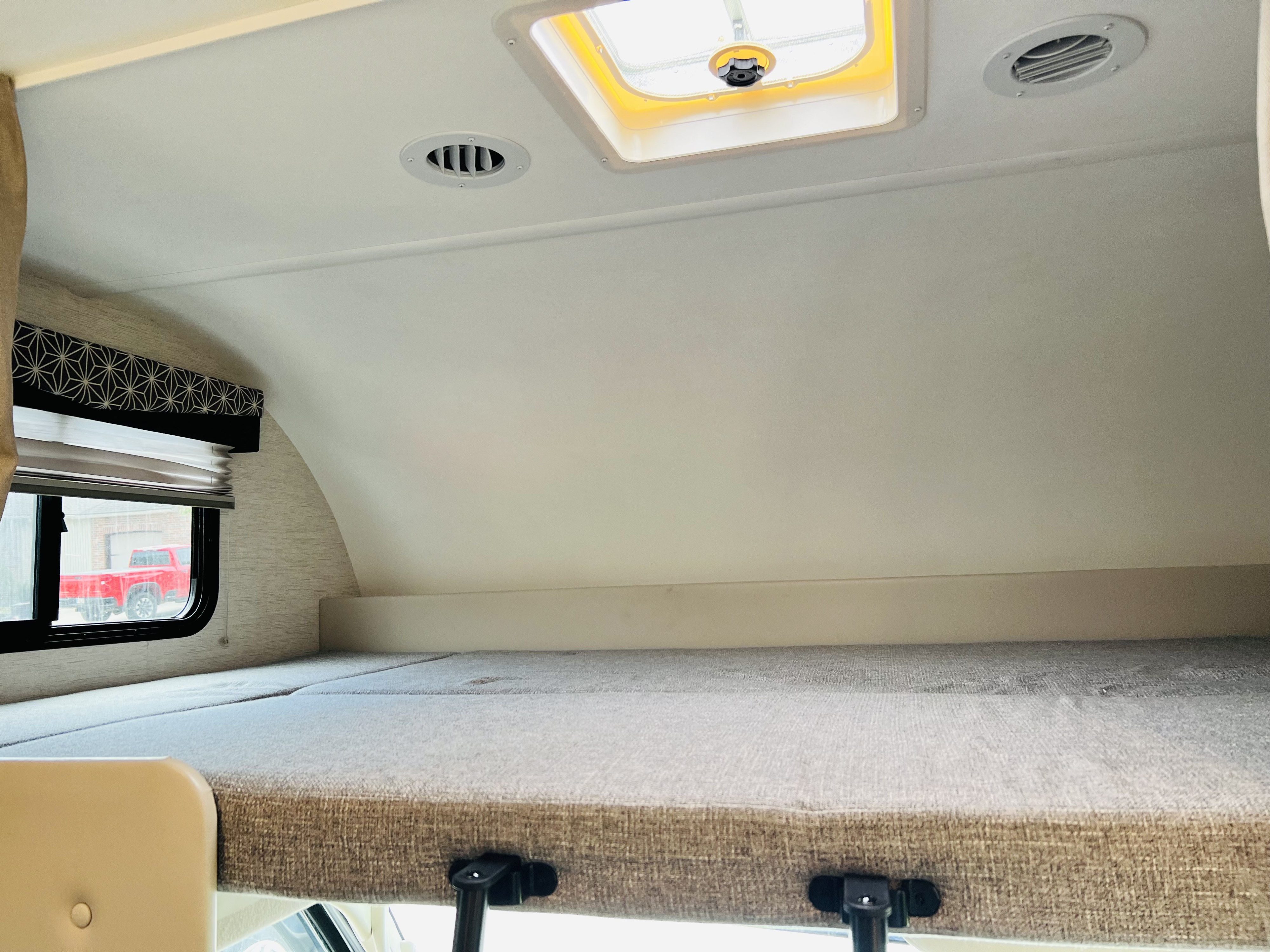 RV rental's spacious cab-over bunk with a light mattress, window, and ceiling vents, offering a cozy sleeping area.. Thor Freedom Elite 2024