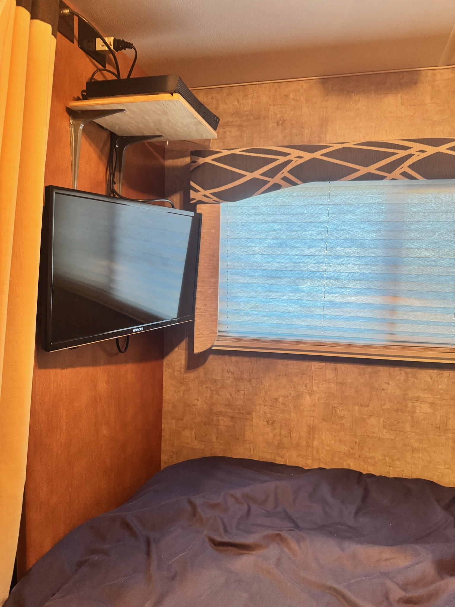 Inside an RV rental: Compact bedroom with a mounted TV, entertainment shelf, comfy bed, and window with blinds.. Winnebago Minnie Winnie 2015