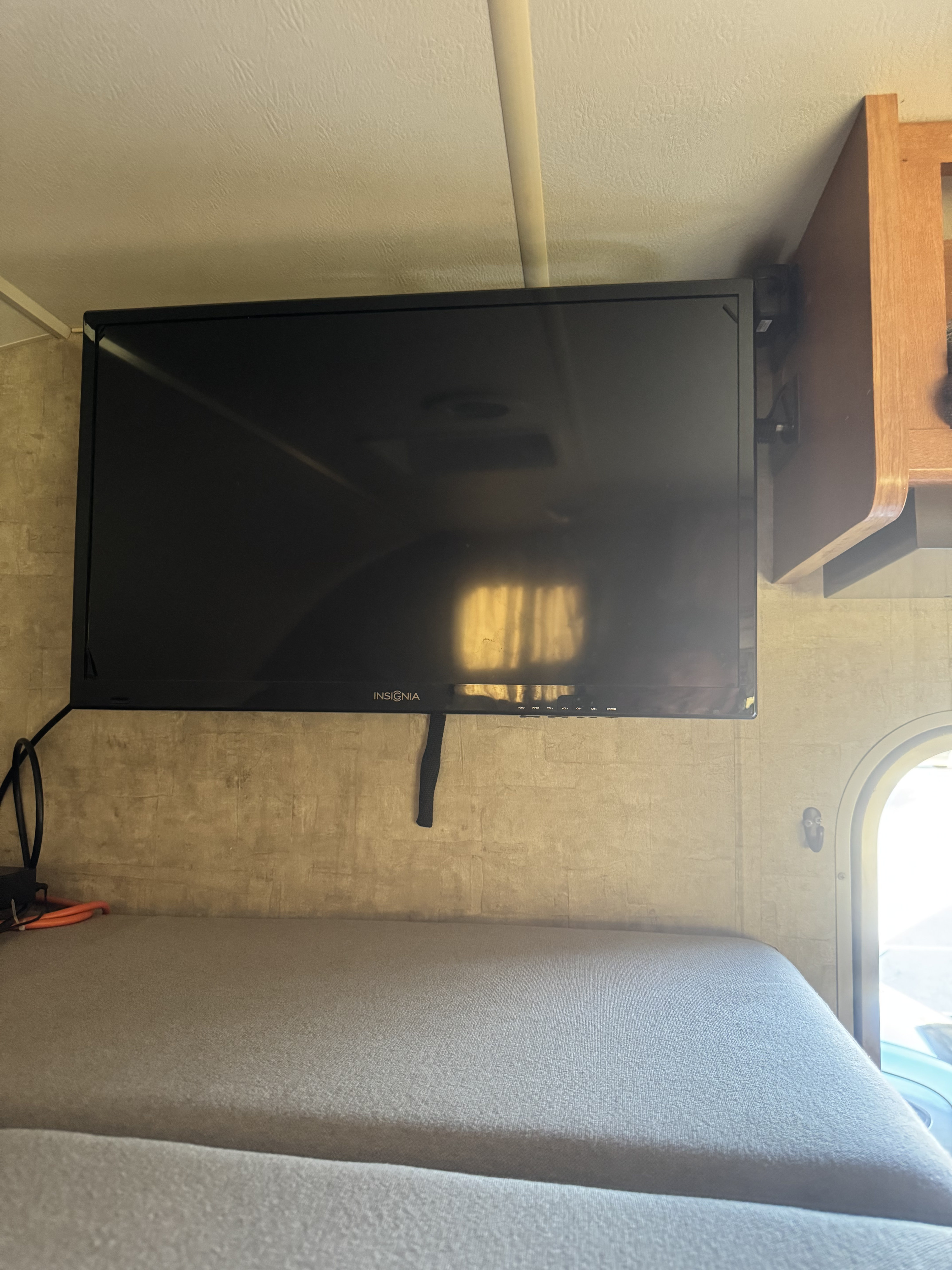 Inside an RV rental: a mounted flat-screen TV above a comfortable cushioned seating area, with a cabinet and exterior view visible.. Winnebago Minnie Winnie 2015