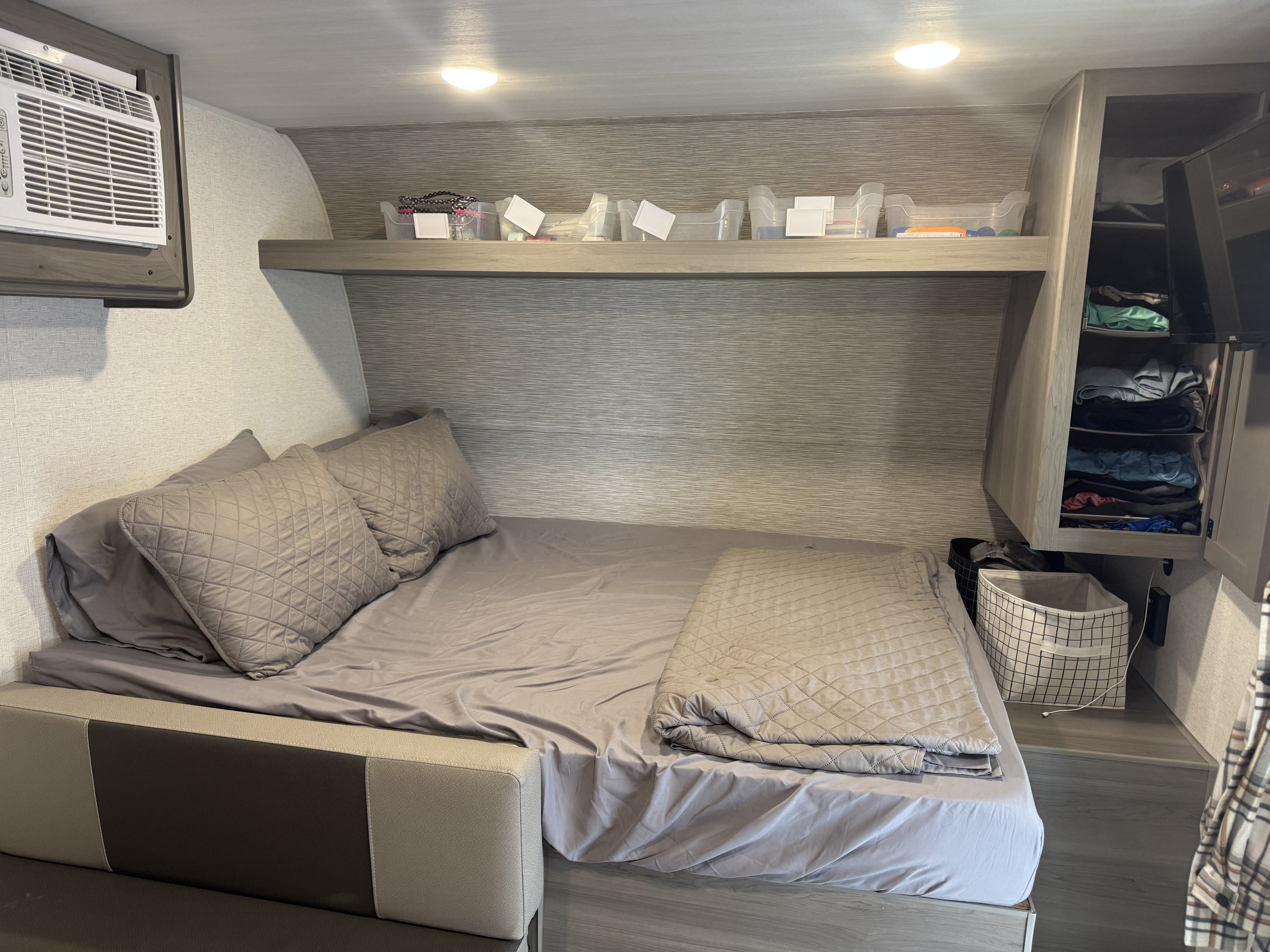Interior of an RV rental: a compact bedroom features a bed with gray bedding, overhead storage, and an AC unit.. Keystone Hideout Sport 175 BH 2025