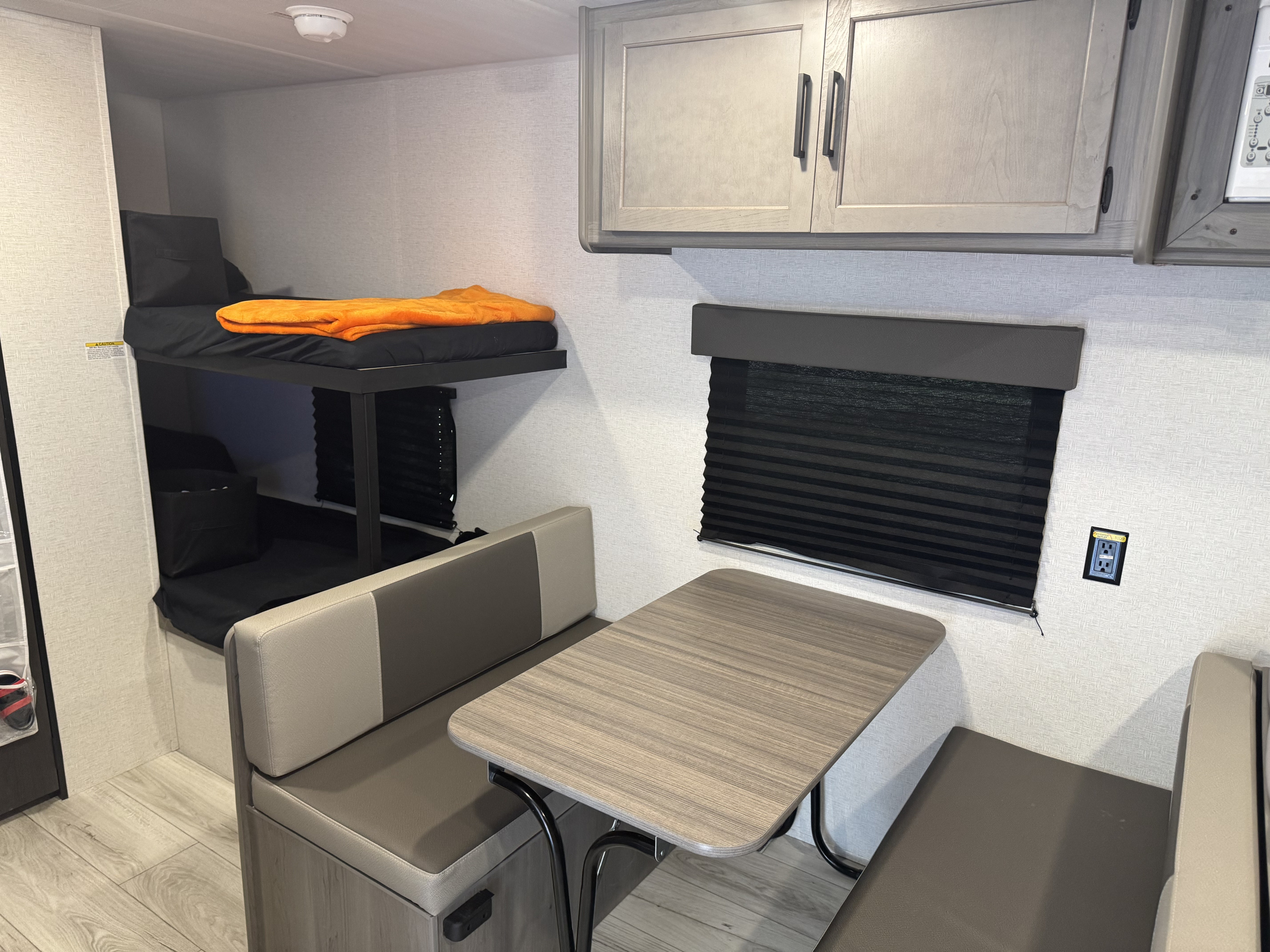 Interior of an RV rental featuring a dinette with bench seating, bunk beds with an orange blanket, and overhead cabinets.. Keystone Hideout Sport 175 BH 2025