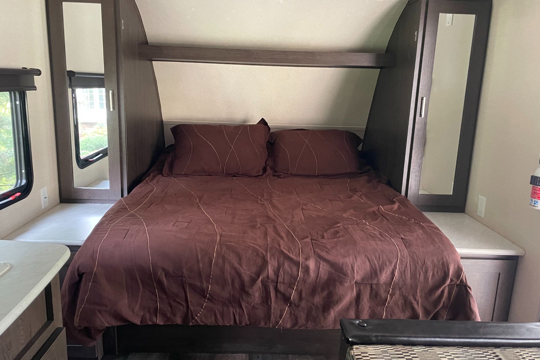 This cozy RV rental bedroom features a comfortable bed with brown bedding, built-in mirrored wardrobes, and side tables, ideal for travel.. Forest River Wildwood X-Lite 2018
