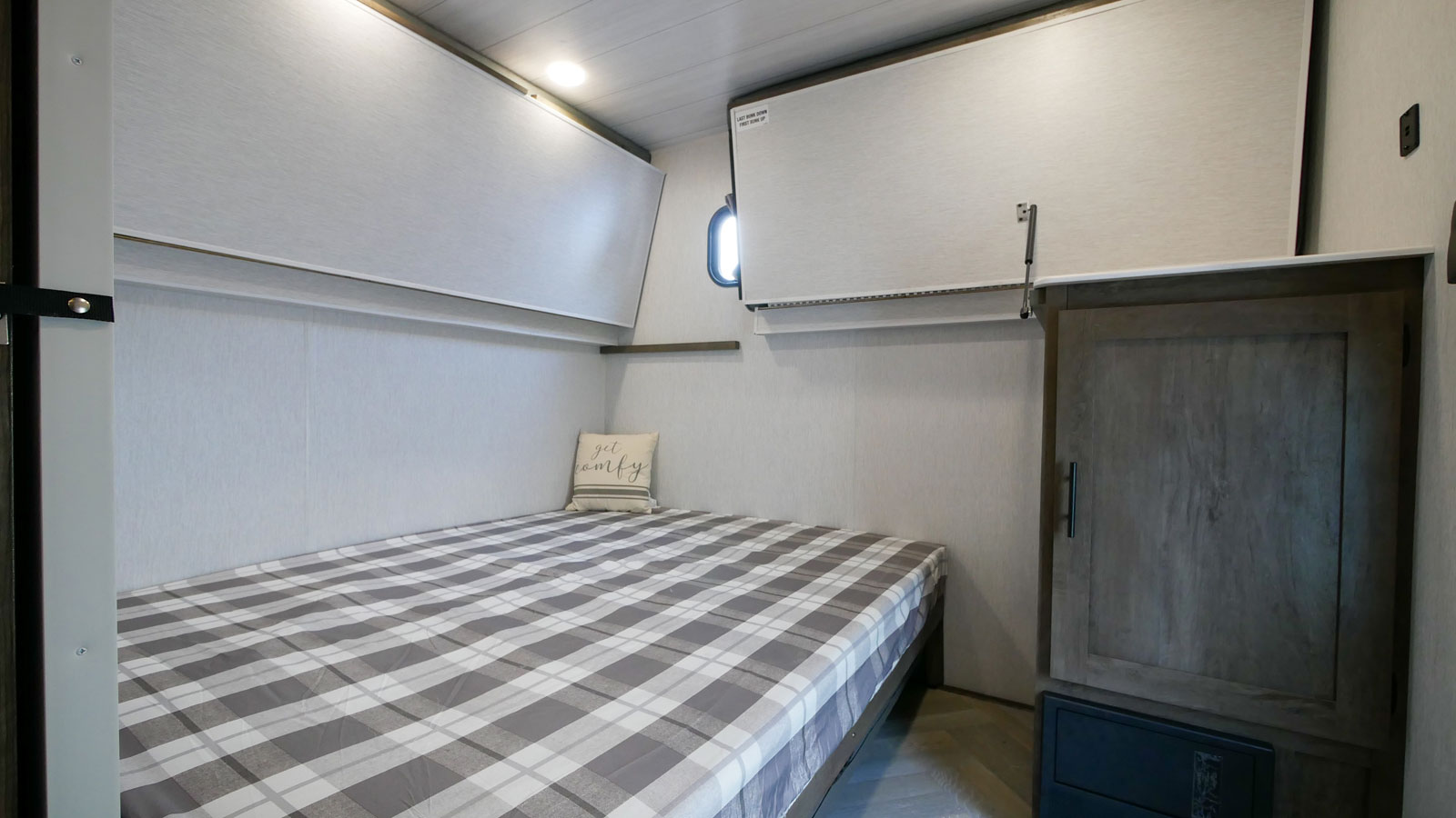 Cozy RV rental bedroom featuring a plaid bed, 'get comfy' pillow, small closet, and clever fold-down bunk beds above.. Forest River Wildwood 2021
