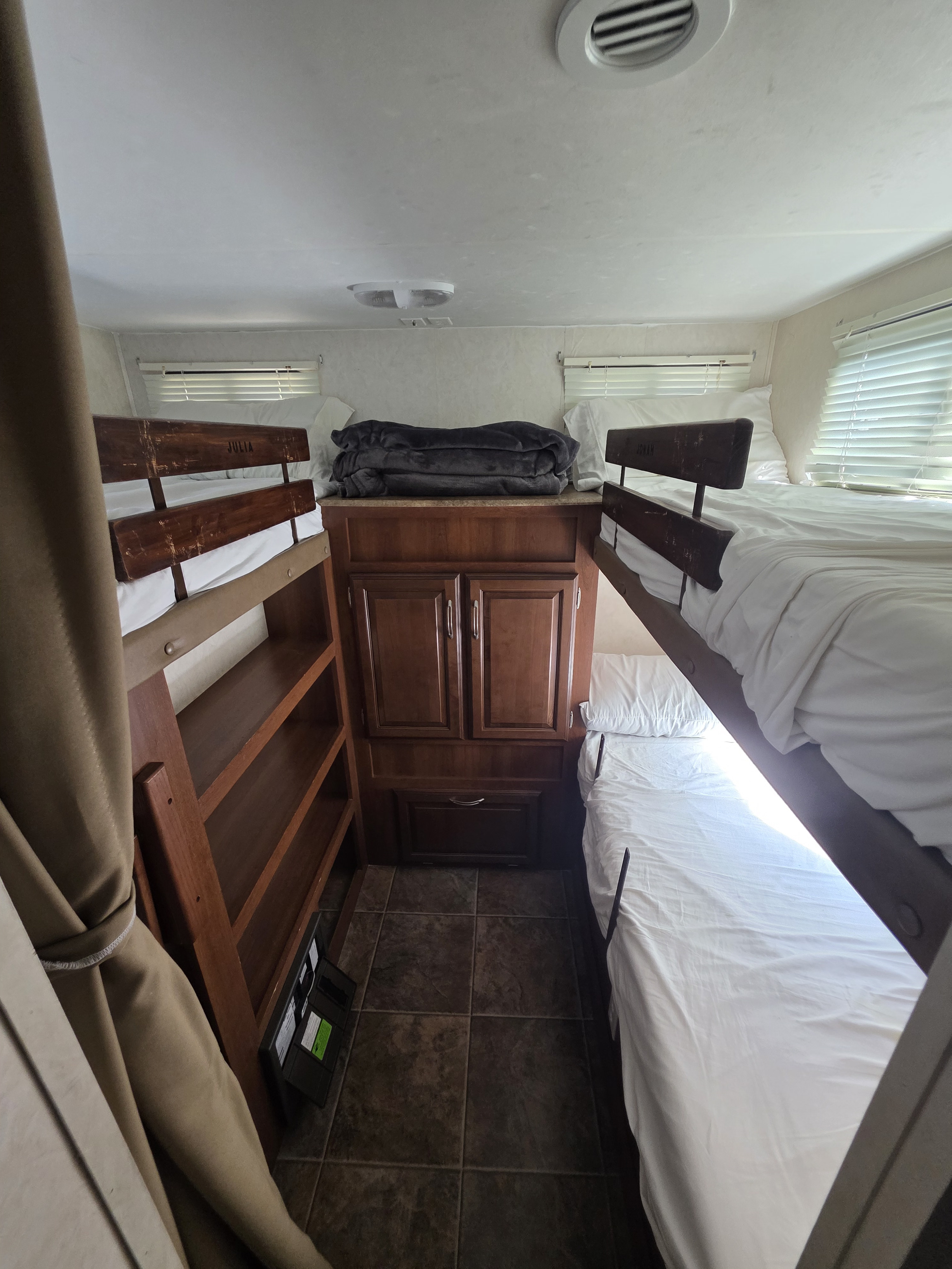 RV rental bunkhouse featuring two sets of wooden bunk beds with white linens, a central storage unit, and windows.. Forest River Coachmen Freedom Express 2012