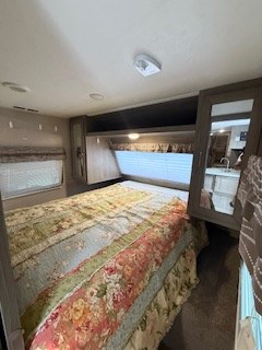 Cozy RV rental bedroom: queen bed with floral quilt, windows, and mirrored cabinets. Your comfortable escape awaits.. Forest River Palomino Puma XLE 2020