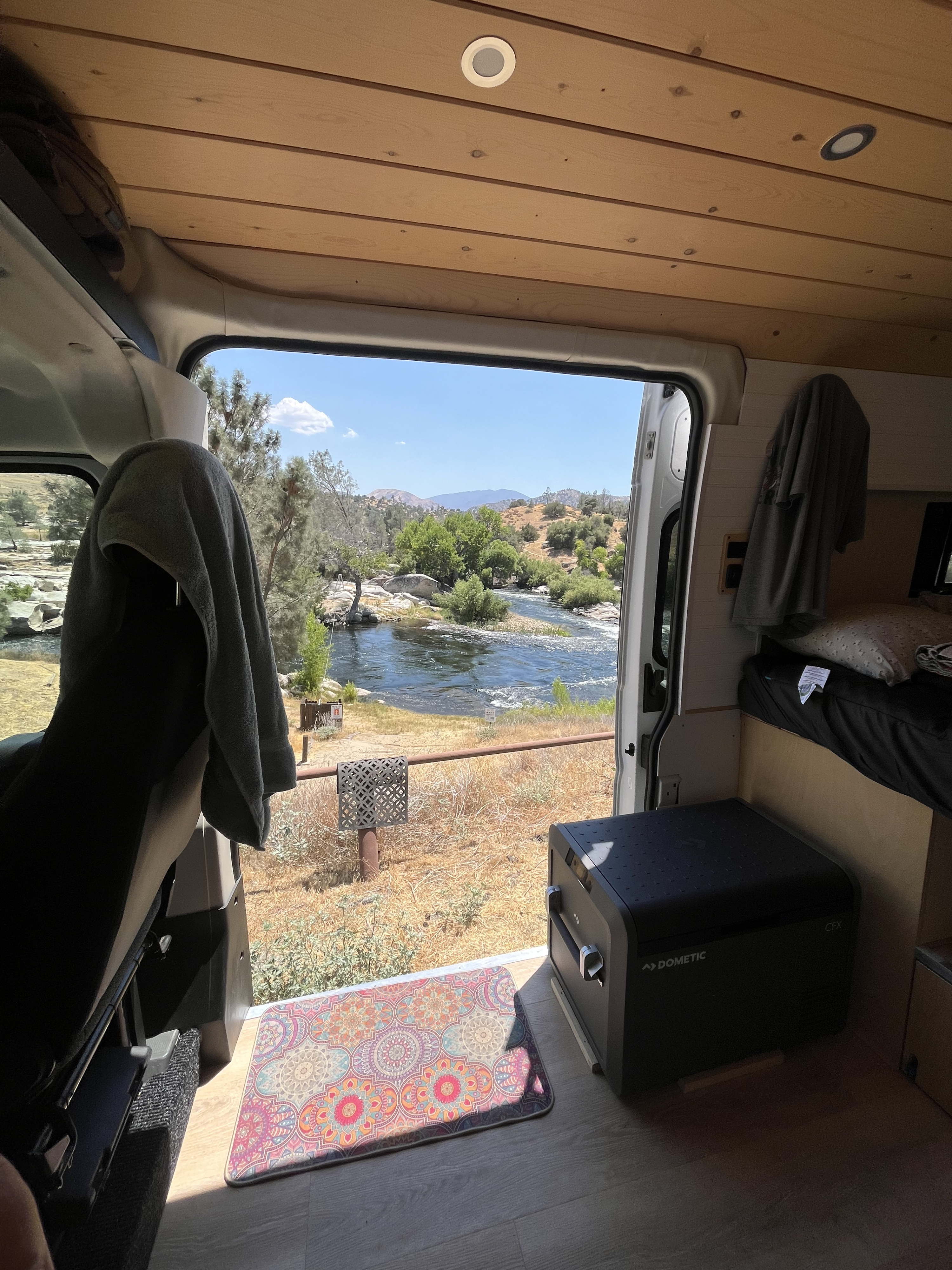 RV rental van interior: a cozy setup overlooking a beautiful river and distant mountains. Dometic fridge.. Dodge Ram 1500 2021