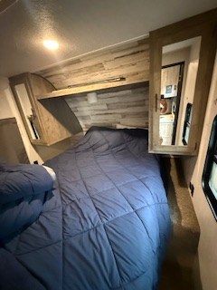 This comfortable RV rental bedroom features a large bed with blue bedding, built-in storage, and wood-look paneling. Ideal for your next trip.. Forest River Palomino Puma XLE Toy Hauler 2020