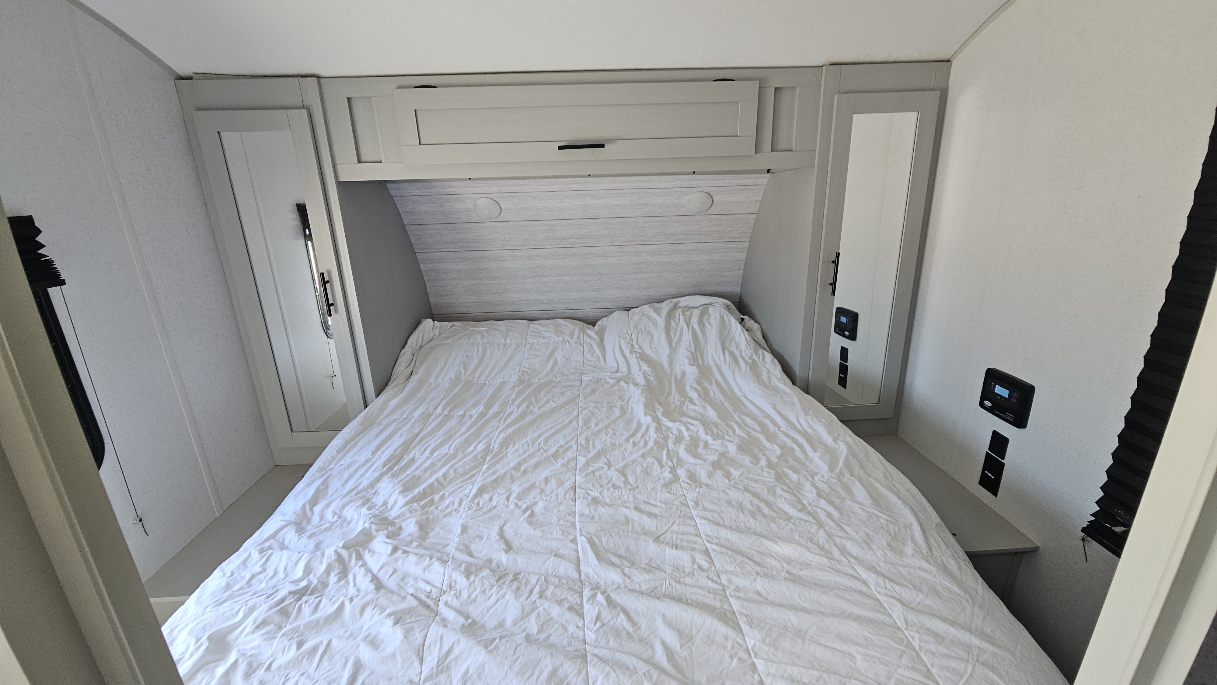 An RV rental bedroom with a white bed, overhead storage, mirrored cabinets, and wall-mounted controls for a cozy journey.. Forest River Wildwood 2022