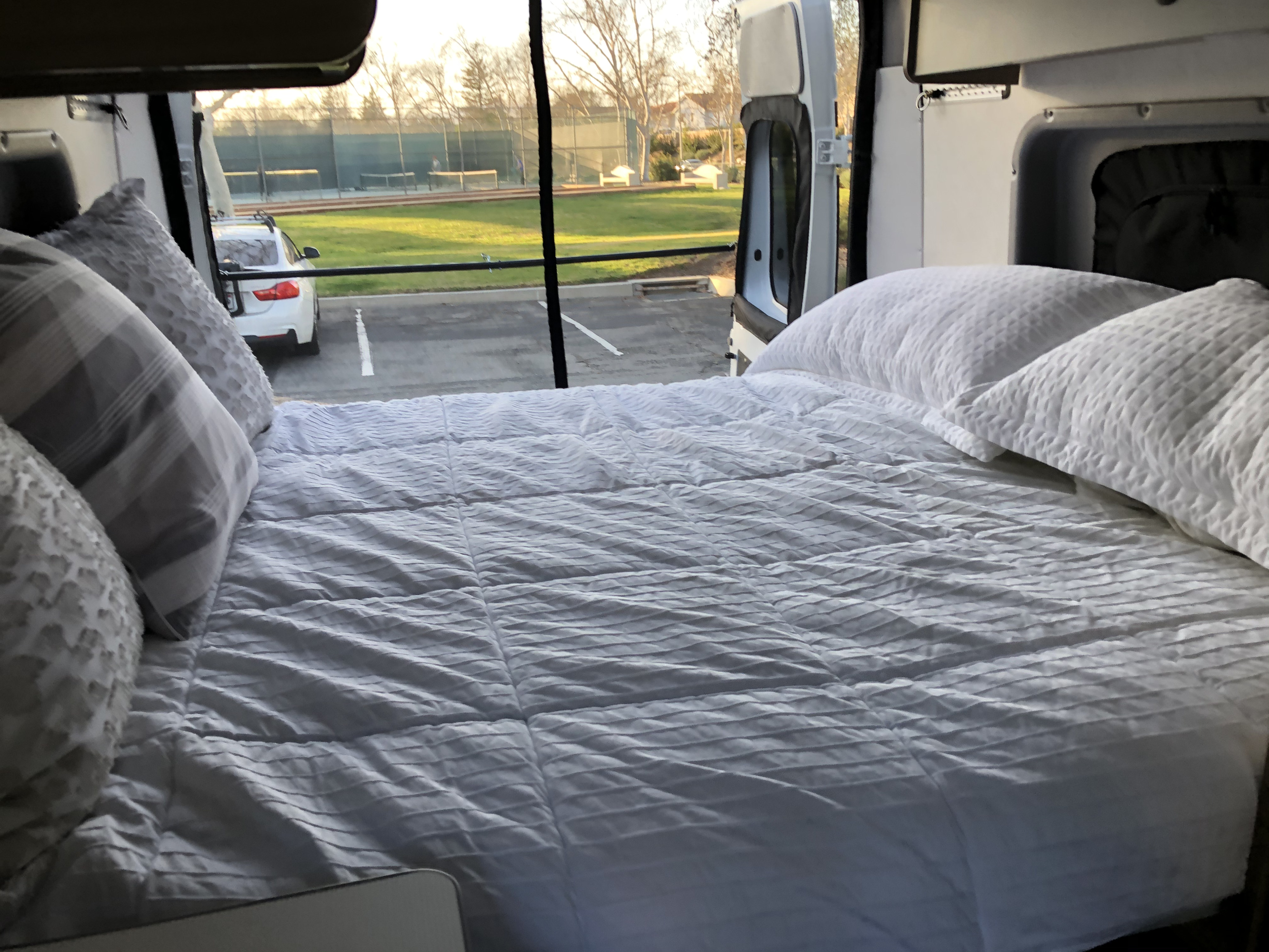 Inside an RV rental: Relax on this cozy bed with an open view of a park and tennis courts outside.. Winnebago Solis 2021