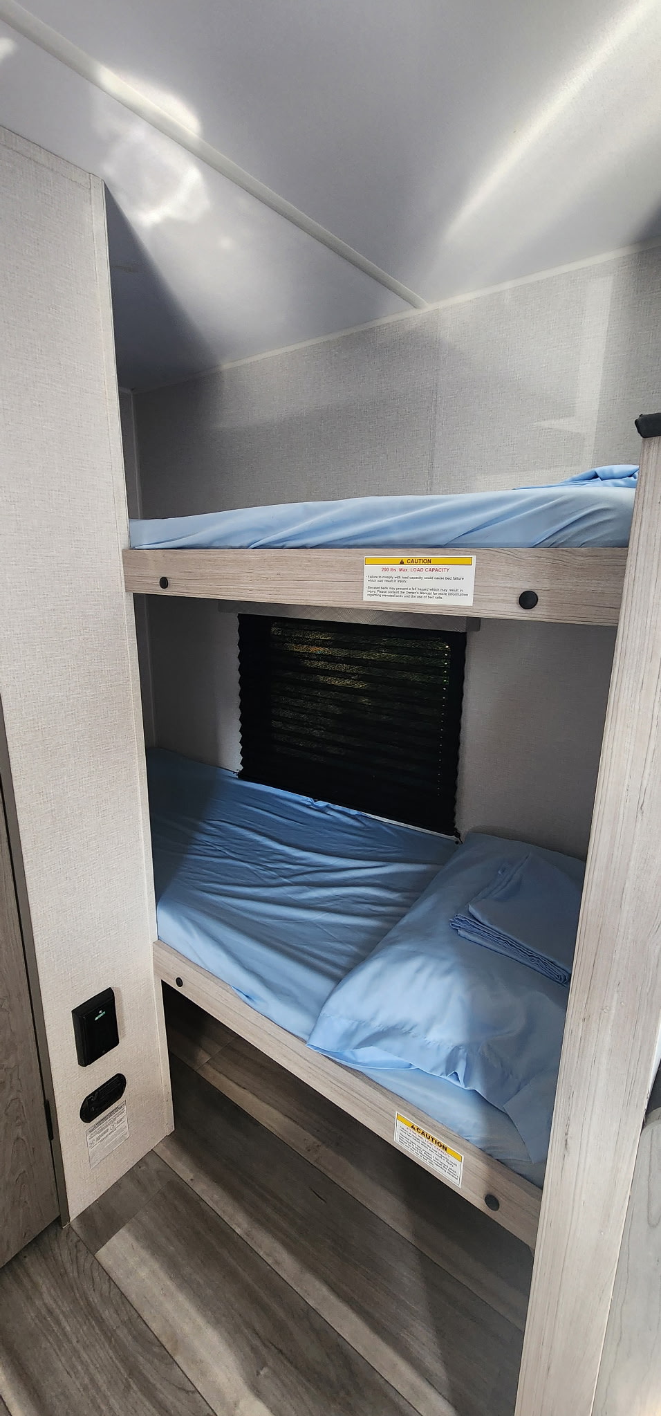 Bunk beds in an rv rental, made with light blue sheets. A 200 lbs max load caution sticker is on the upper bunk frame.. Heartland Pioneer 2025