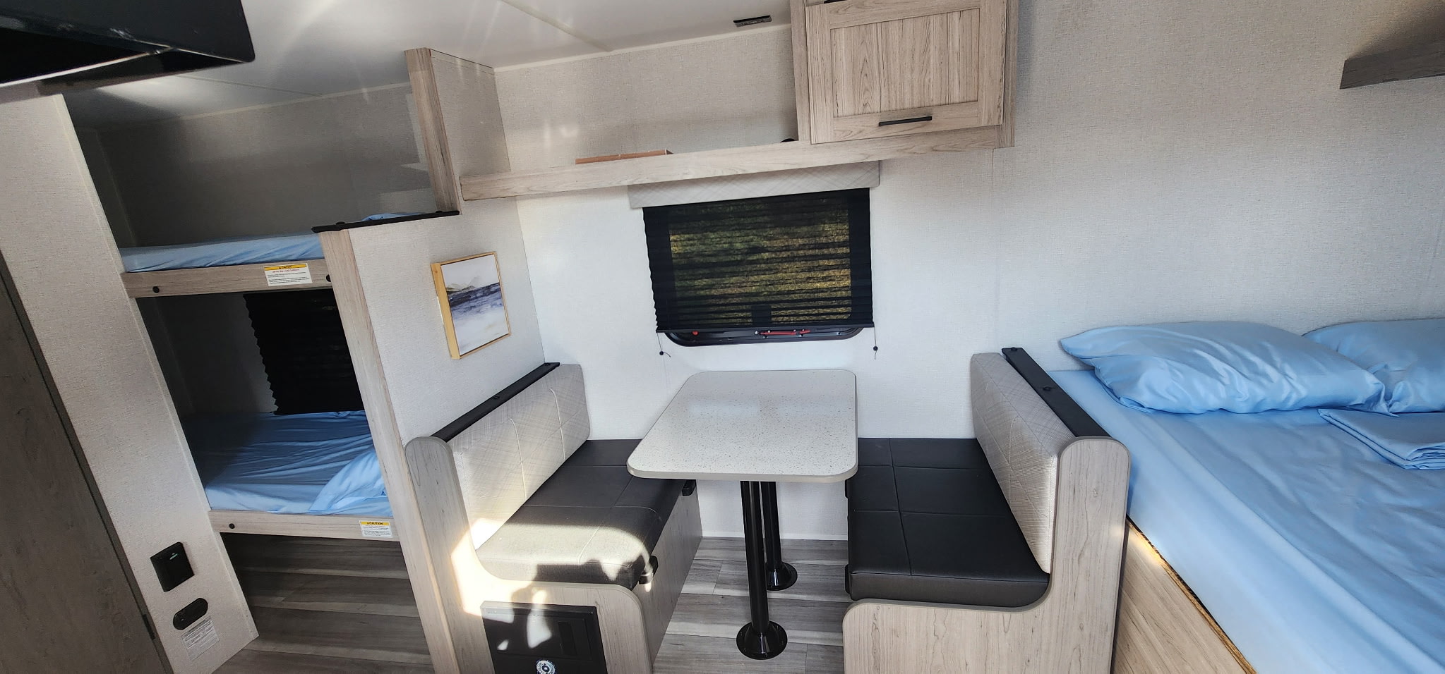 RV rental's inviting interior: bunk beds, a dinette table with benches, and a main bed with blue linen.. Heartland Pioneer 2025