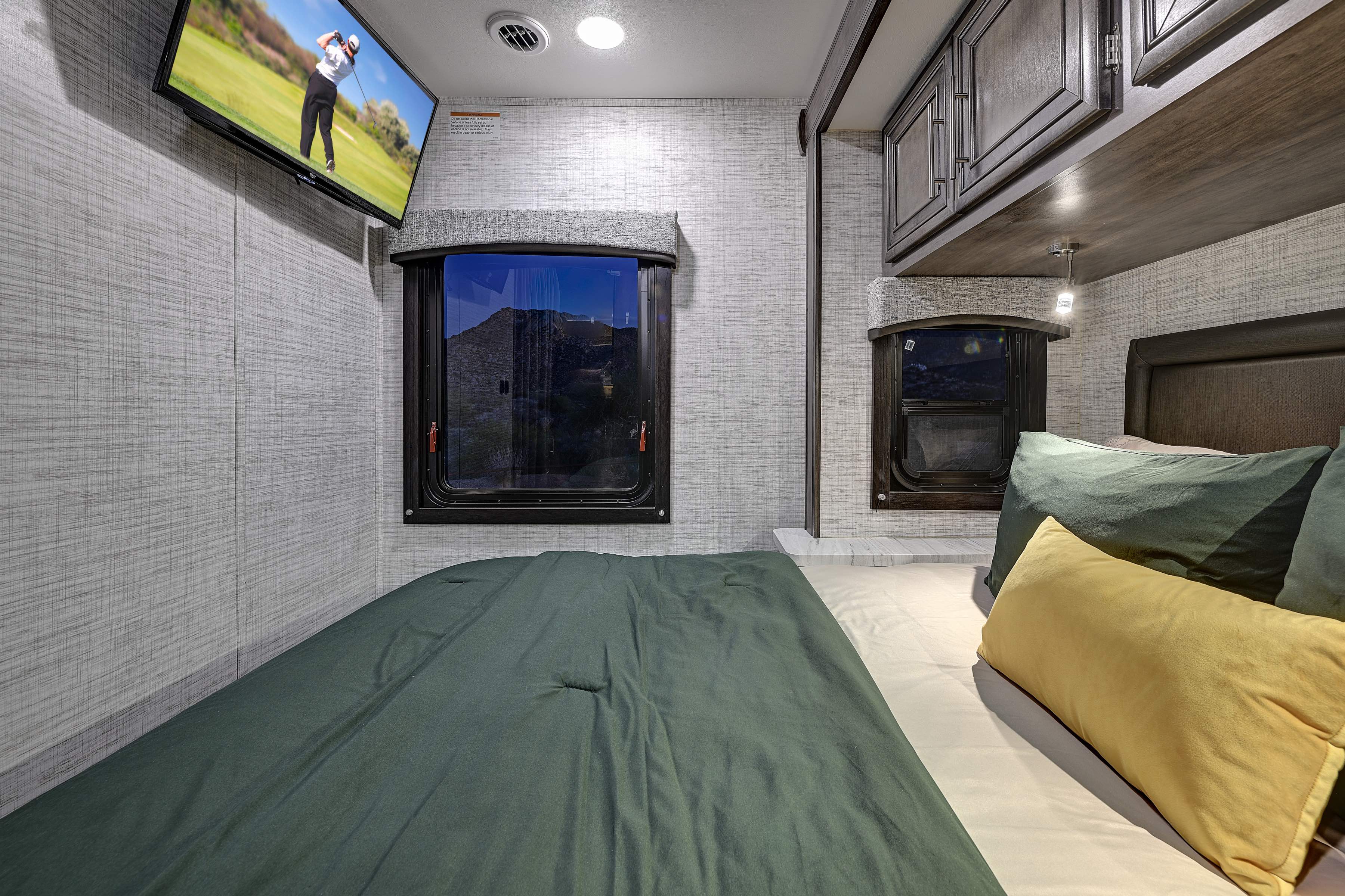 Comfortable RV rental bedroom with bed, two windows, wall-mounted TV, and overhead cabinets for a cozy trip.. Entegra Coach Odyssey SE 2024