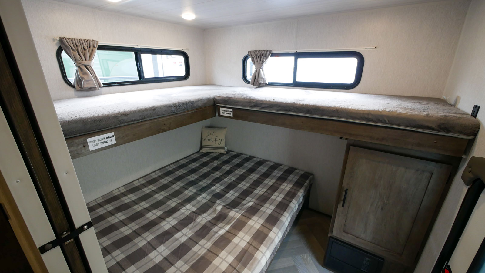 Interior of an rv rental featuring L-shaped bunk beds with windows, a comfy bottom bed, and storage.. Forest River Wildwood 2021