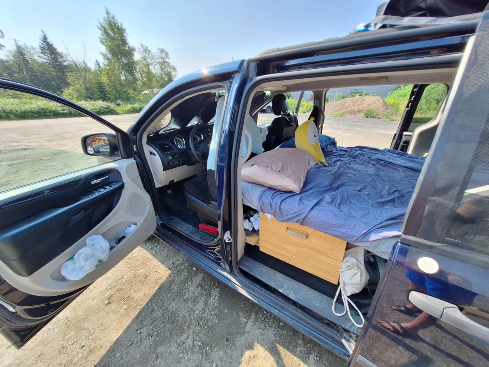 Inside a converted minivan, a cozy bed with under-bed storage, like an RV rental for a comfy road trip.. Dodge Grand Caravan SE 2013