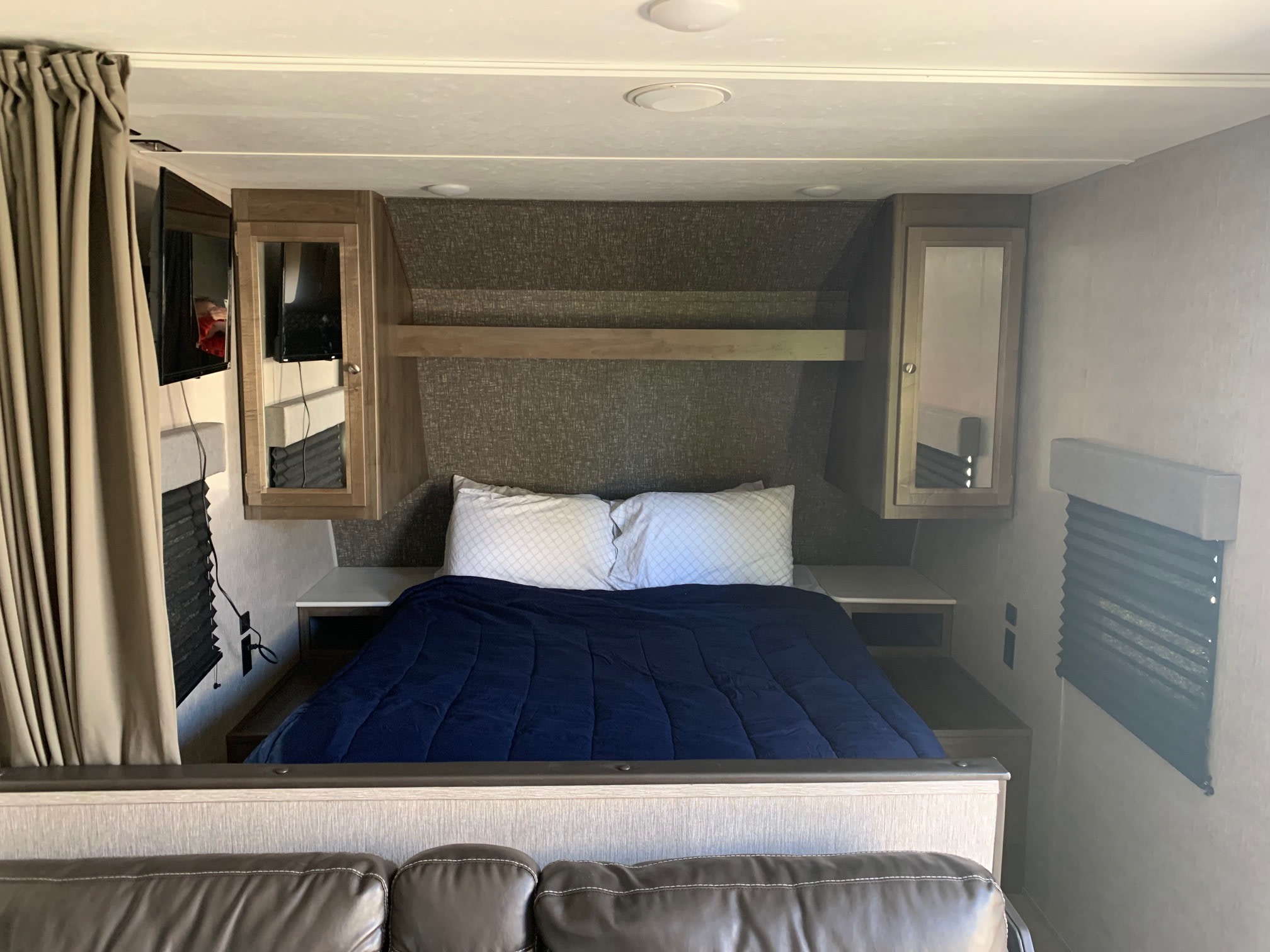 Cozy RV rental interior bedroom featuring a bed with blue comforter, built-in storage, TV, and window blinds.. Dutchman Coleman Lantern LT 2020